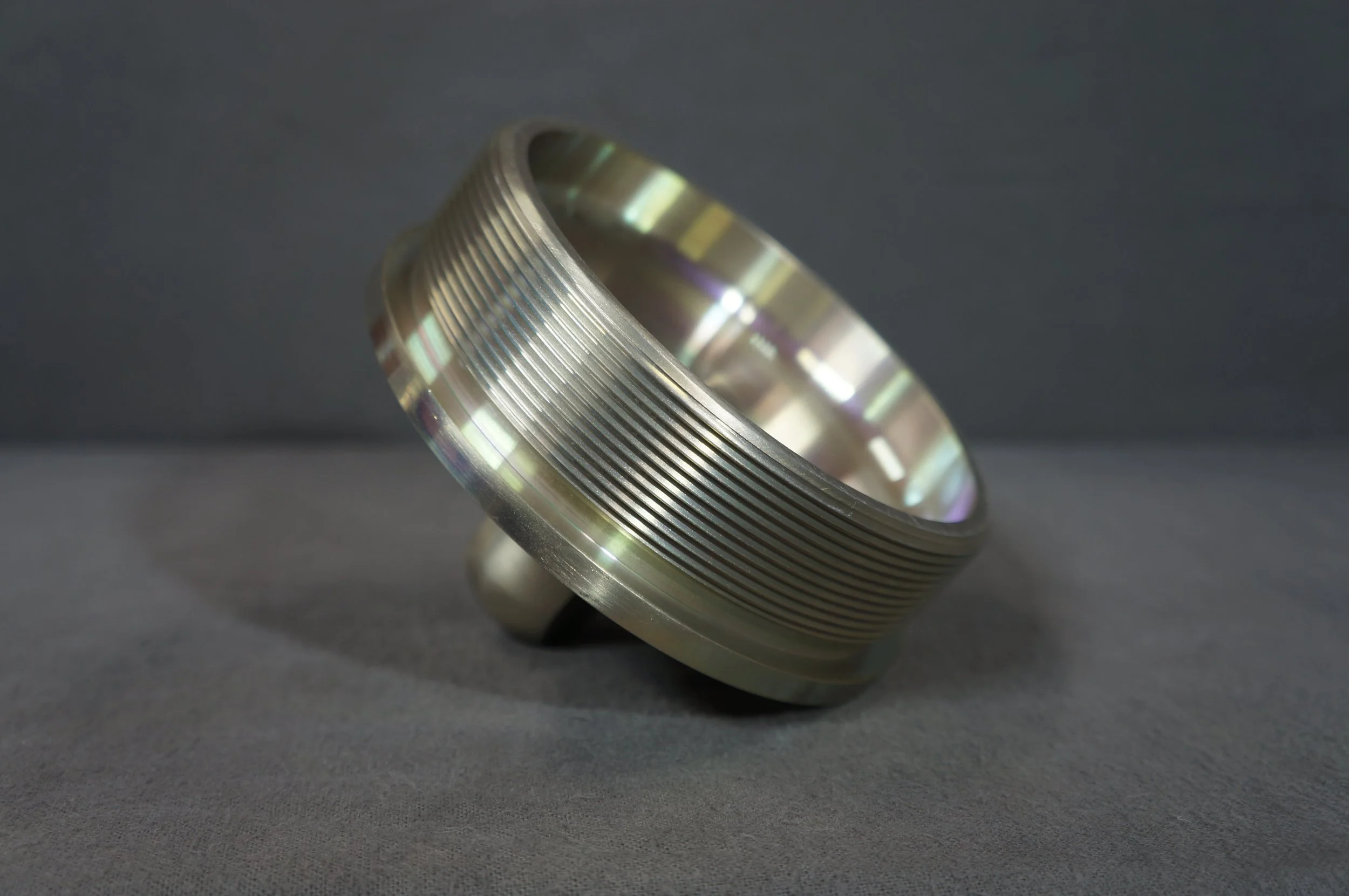 Close-up of a metallic, ridged ring resting on a dark gray surface.