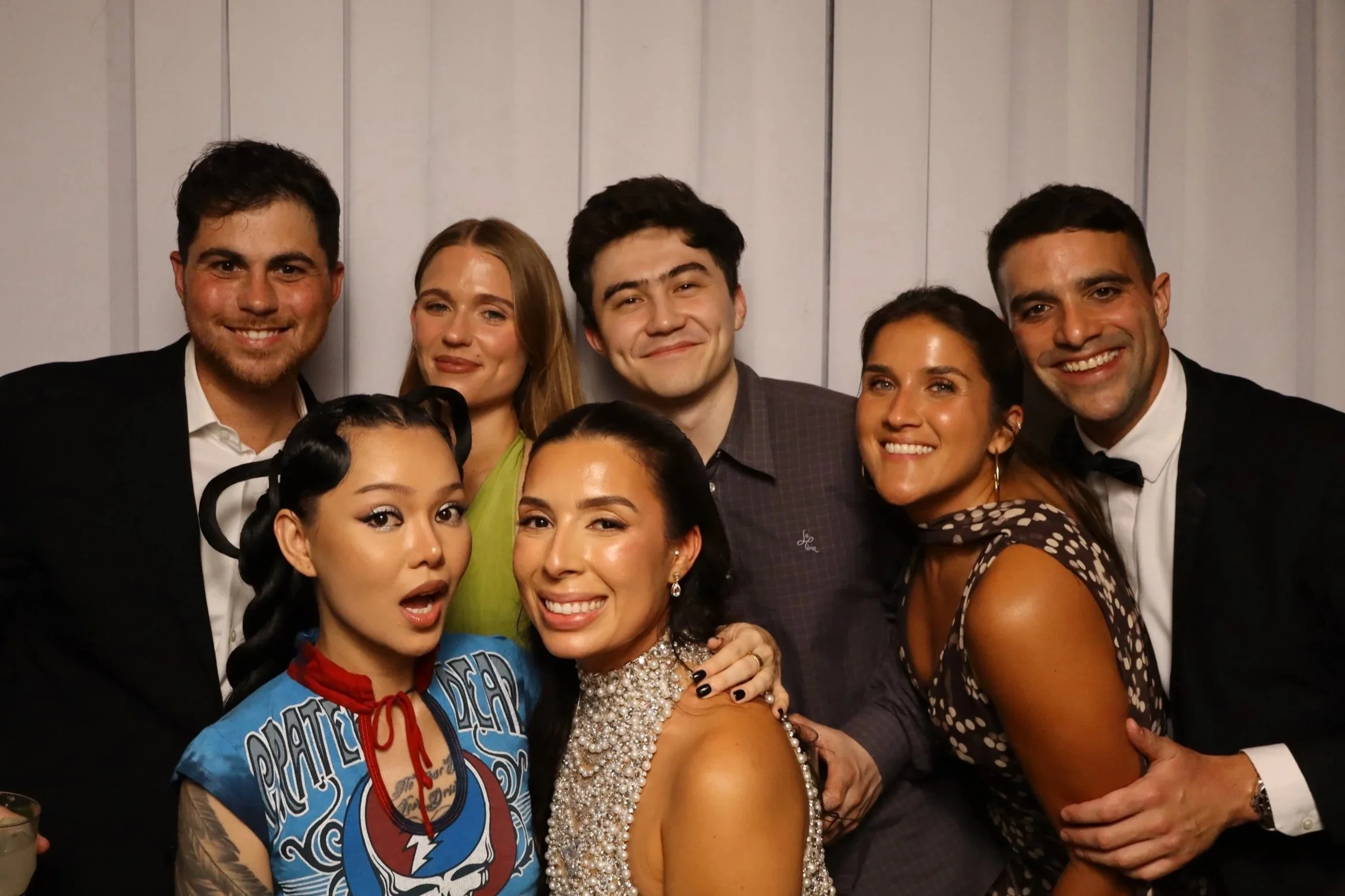 A group of people dressed in formal attire posing happily for a photo in front of a wooden-paneled wall.