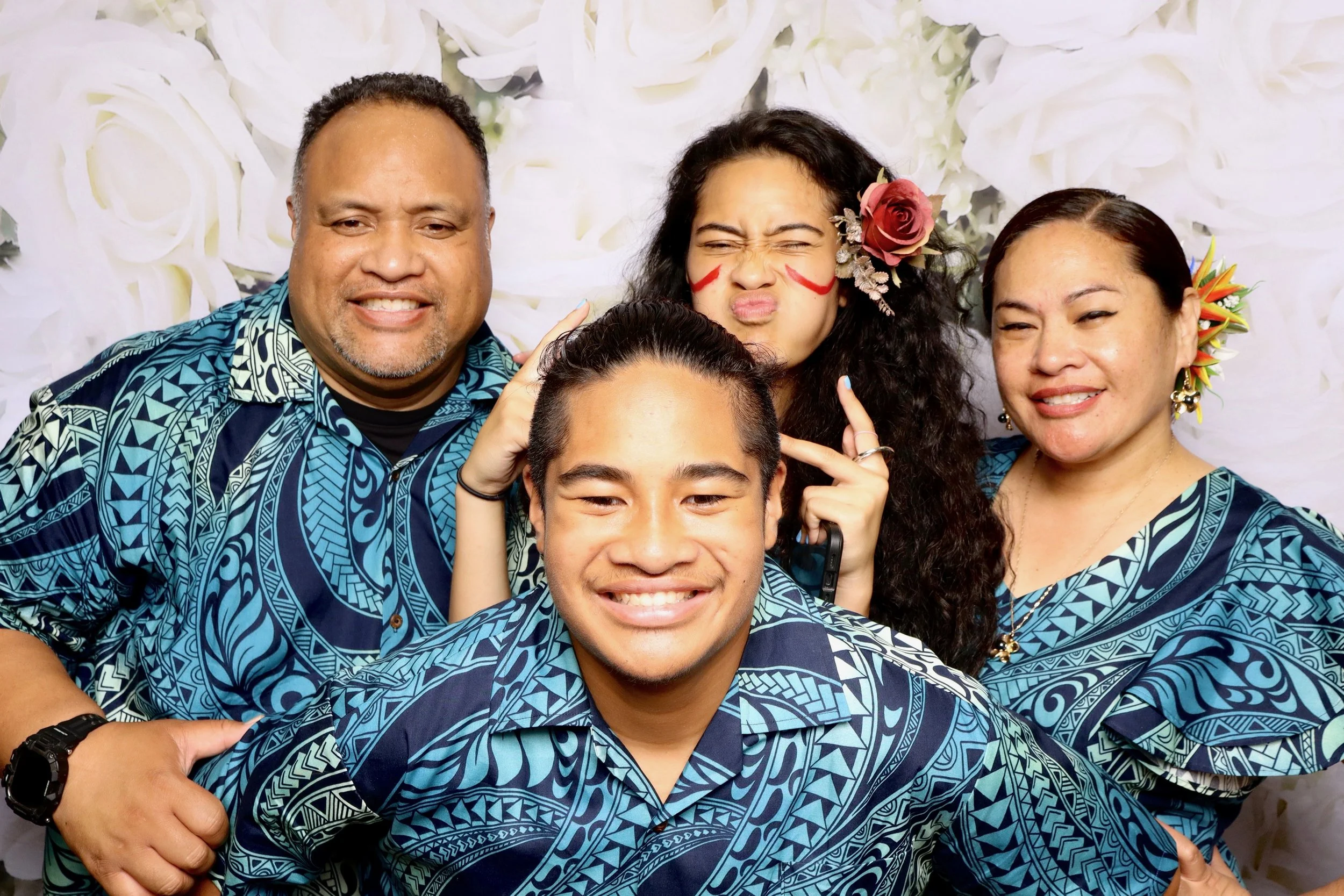 A group of five people taking a selfie together wearing matching blue patterned shirts, with a floral backdrop behind them.