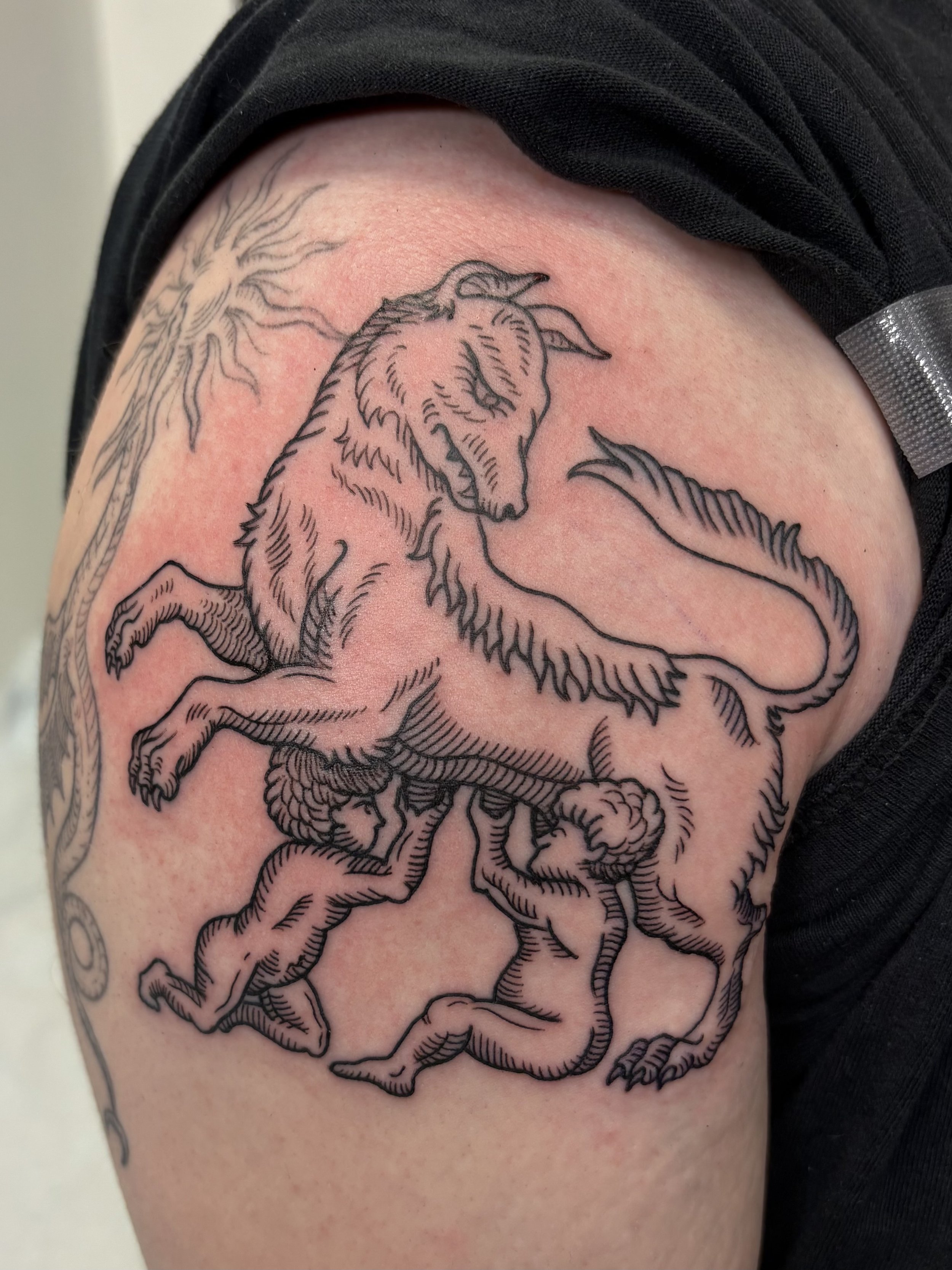 A tattoo of a unicorn with a flowing mane and tail, positioned on a person's upper arm or shoulder, outlined in black ink.