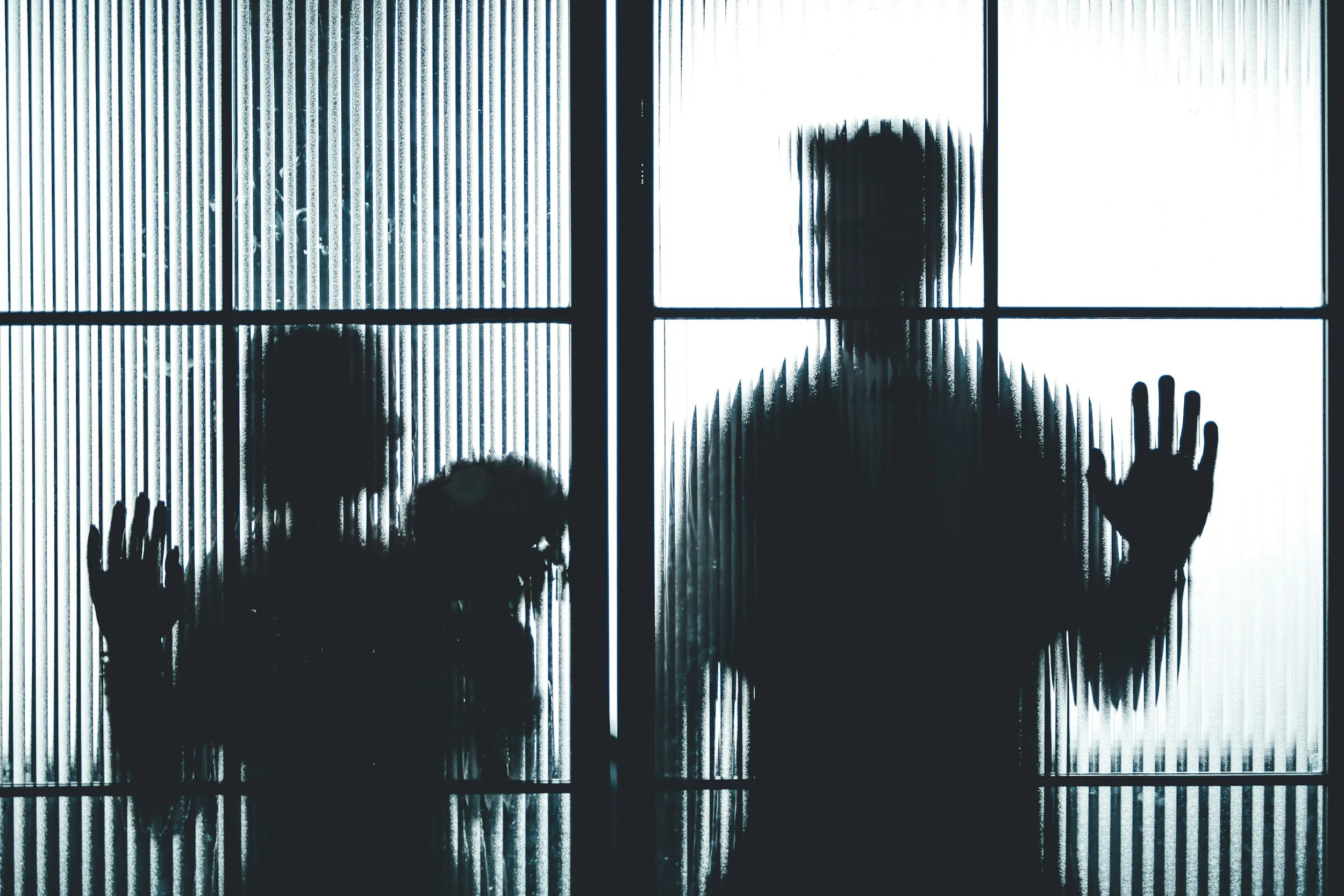 Silhouette of children pressing their hands against the glass of an elevator or glass wall with vertical lines.