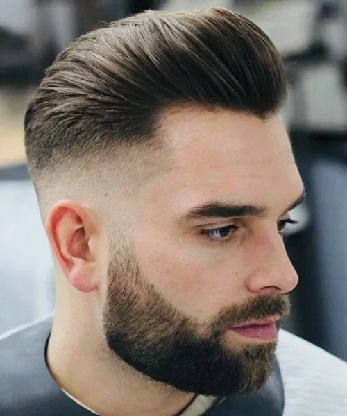 Side profile of a young man with a well-groomed, high fade hairstyle and a full beard.