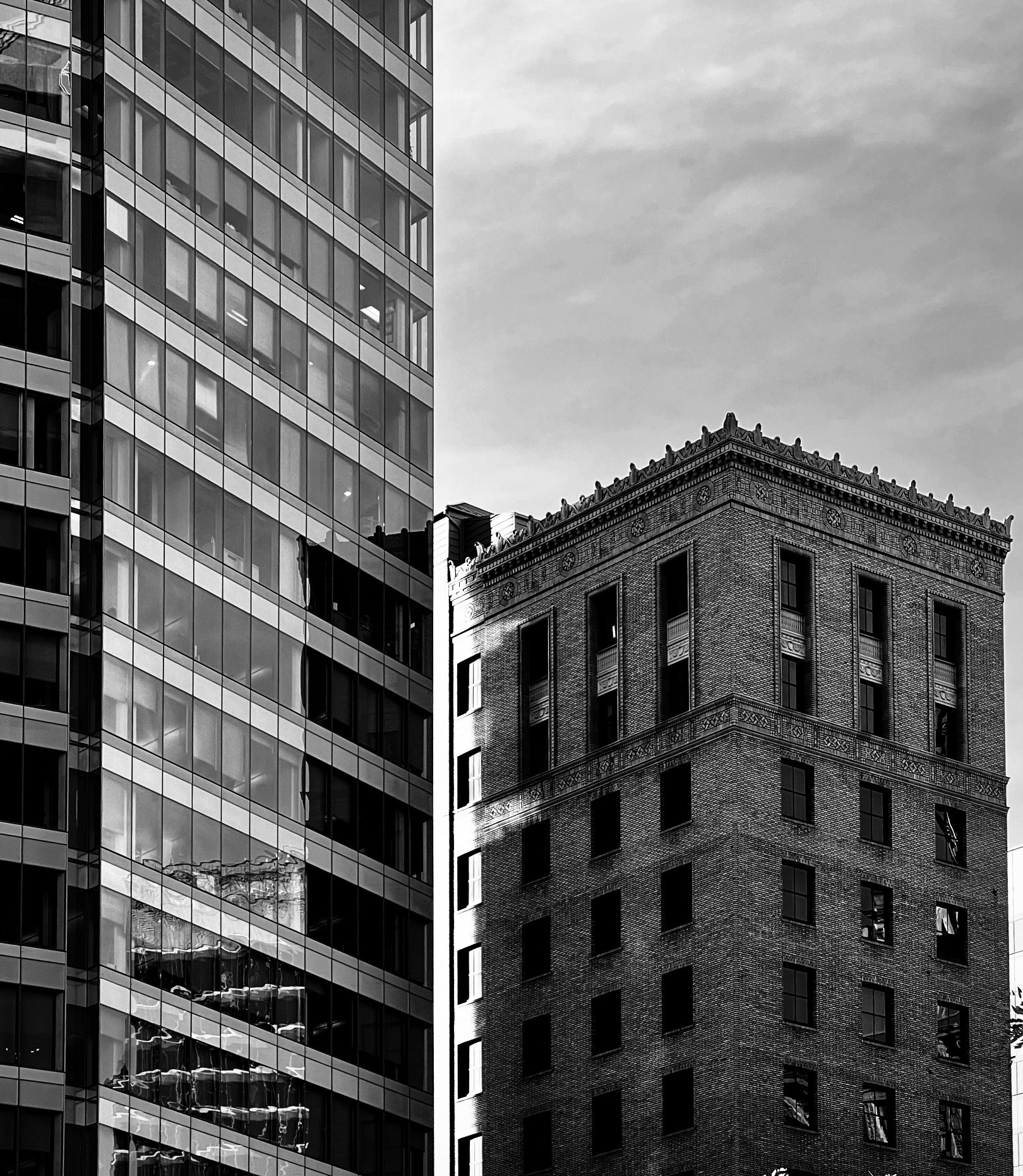 A modern glass curtain-wall tower fills the left half of the frame while an older decorative brick building occupies the right, its ornate cornice facing the sky. Two eras in conversation.