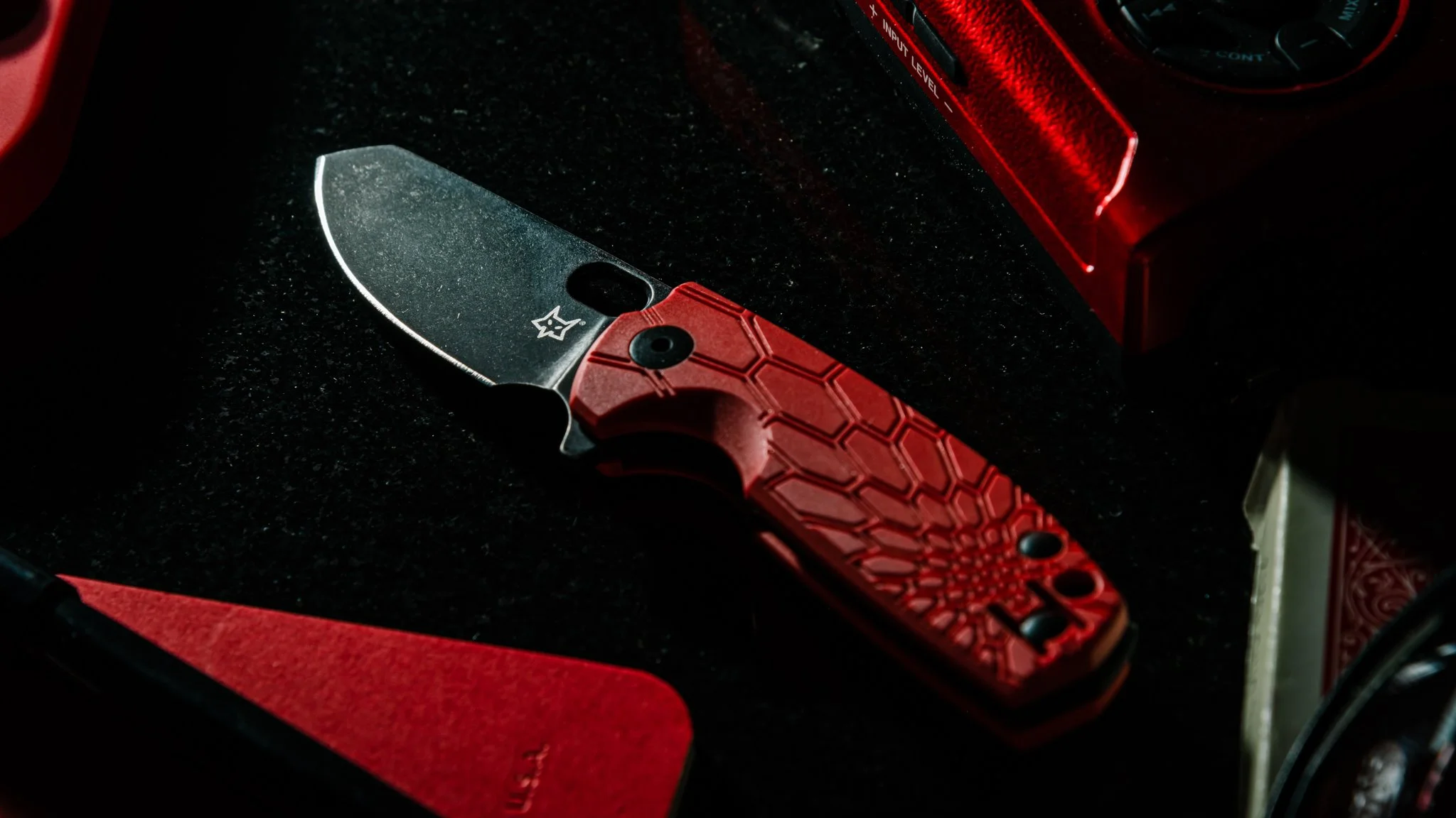 Red handled folding knife on dark surface with red accent lighting moody product photography Utah