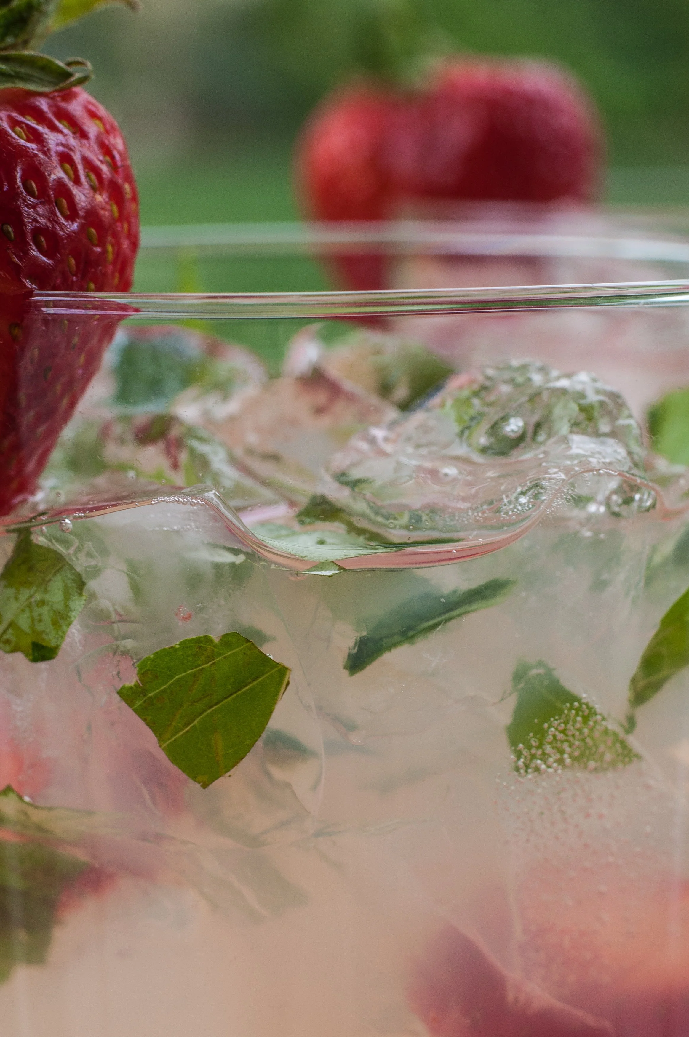 Strawberry mint drink with ice photographed through glass with green bokeh background food photography