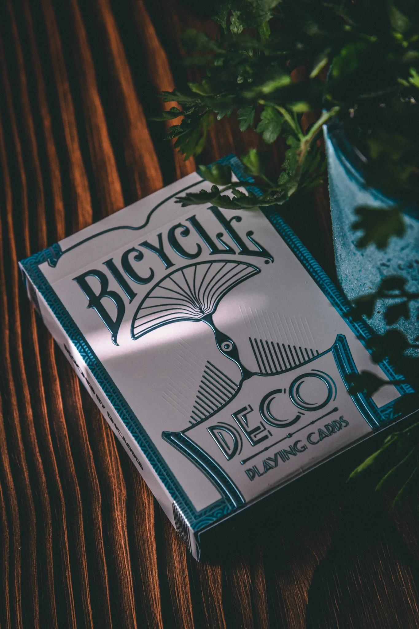 Bicycle Deco playing cards on dark wood surface with green plant lifestyle product photography