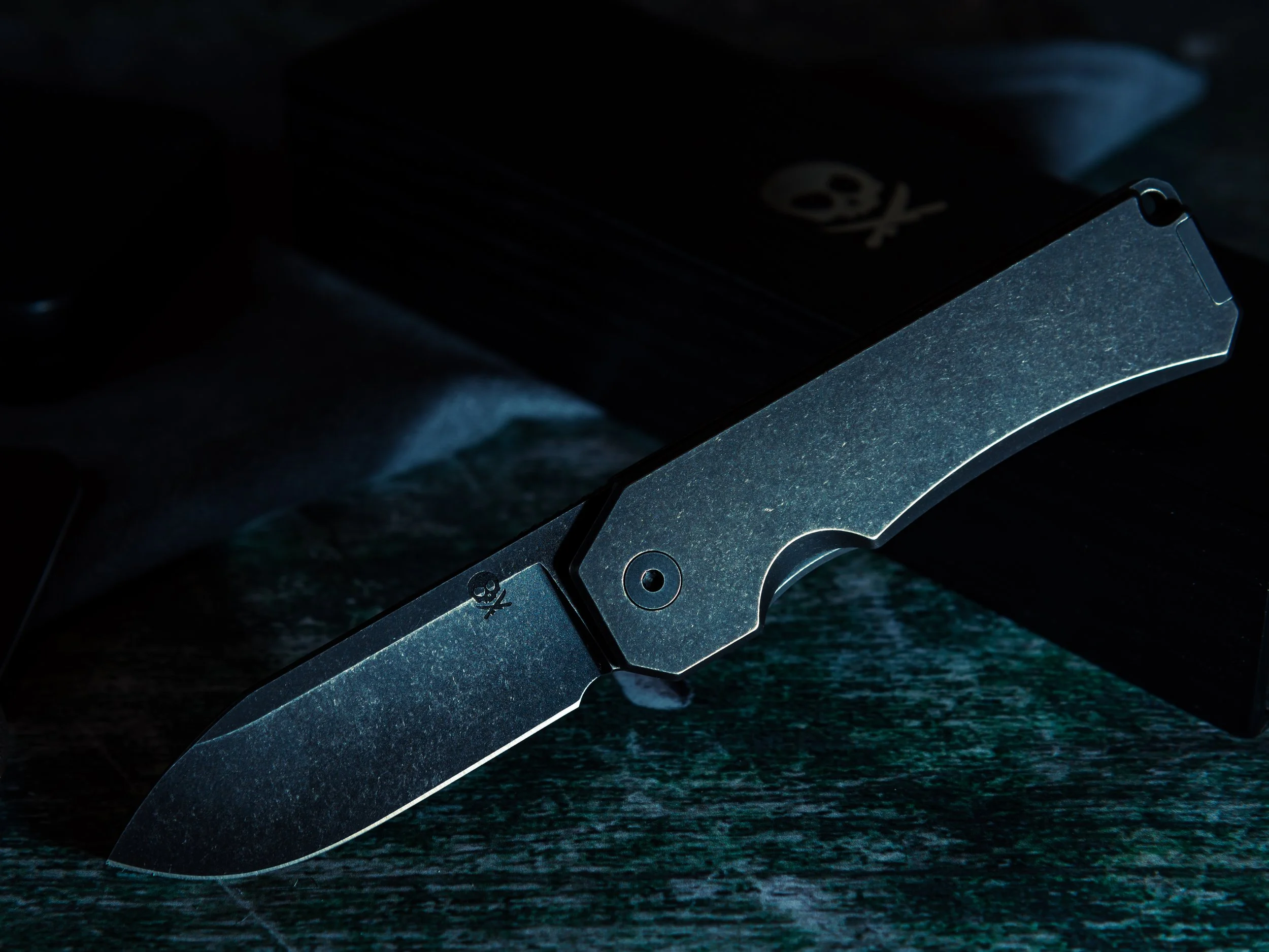 Dark folding knife with textured handle on green marble surface moody product photography Utah