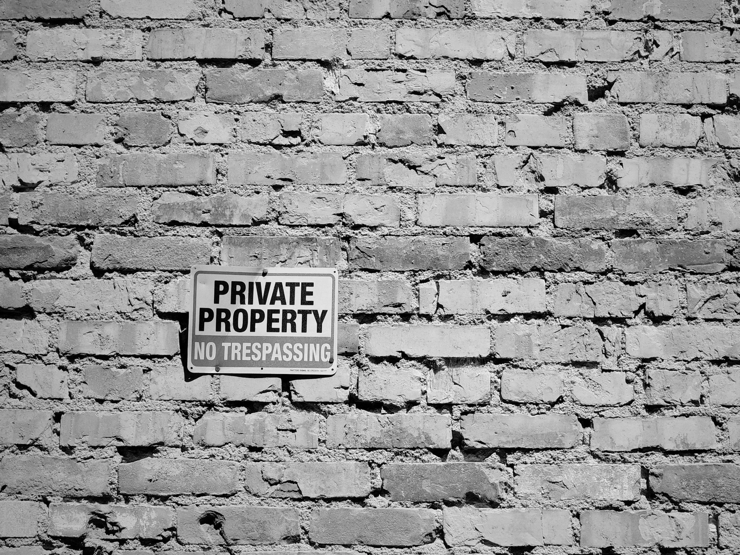A small No Trespassing sign mounted slightly off-center on a weathered brick wall. Nothing else. The wall fills the frame.