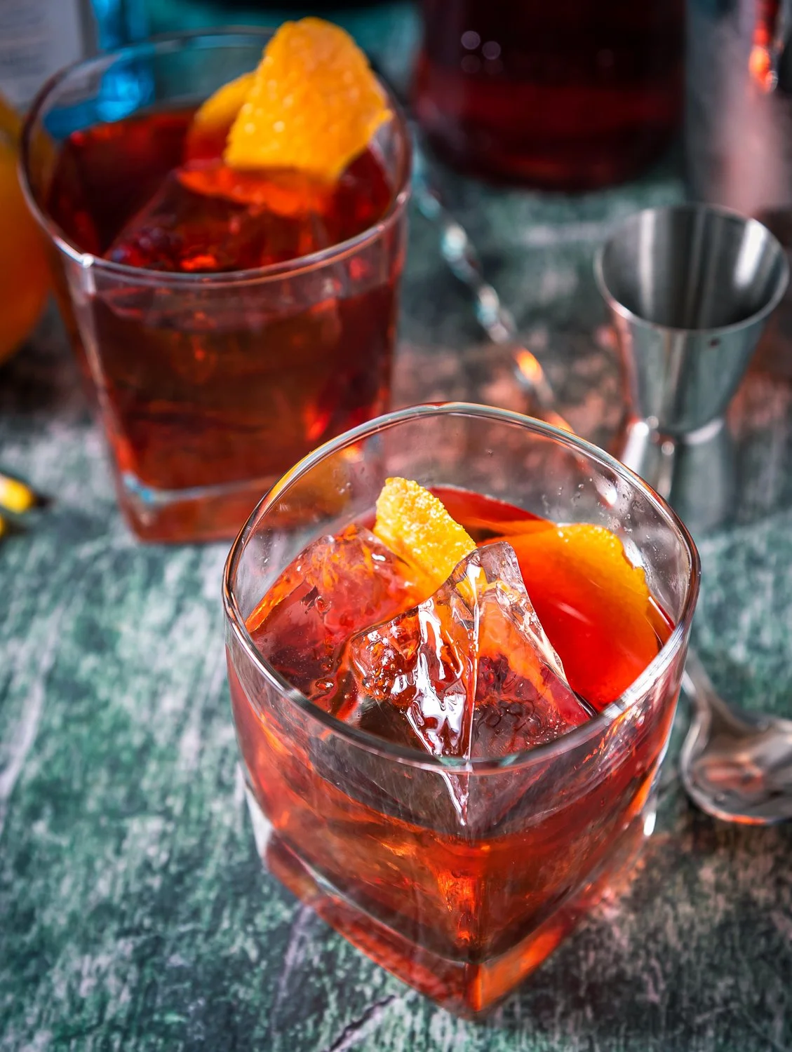 Negroni cocktail with large ice cubes and orange peel garnish on green marble surface Salt Lake City product photography
