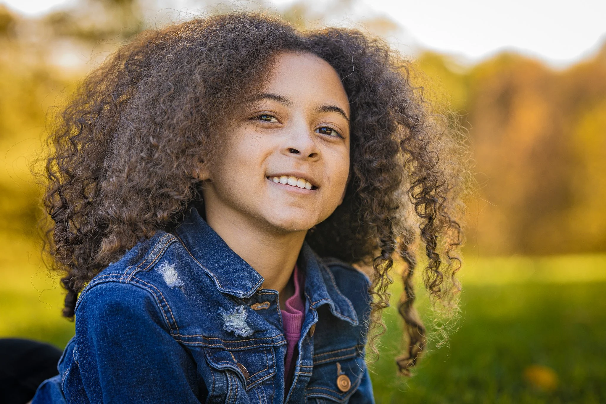 Young girl with curly hair smiling outdoors during fall.