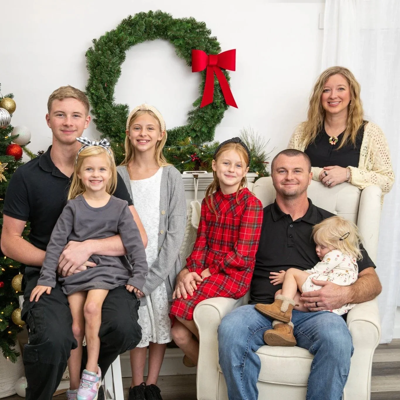 A family of nine celebrating Christmas indoors, posing for a group photo in front of decorated Christmas tree and a holiday wreath.