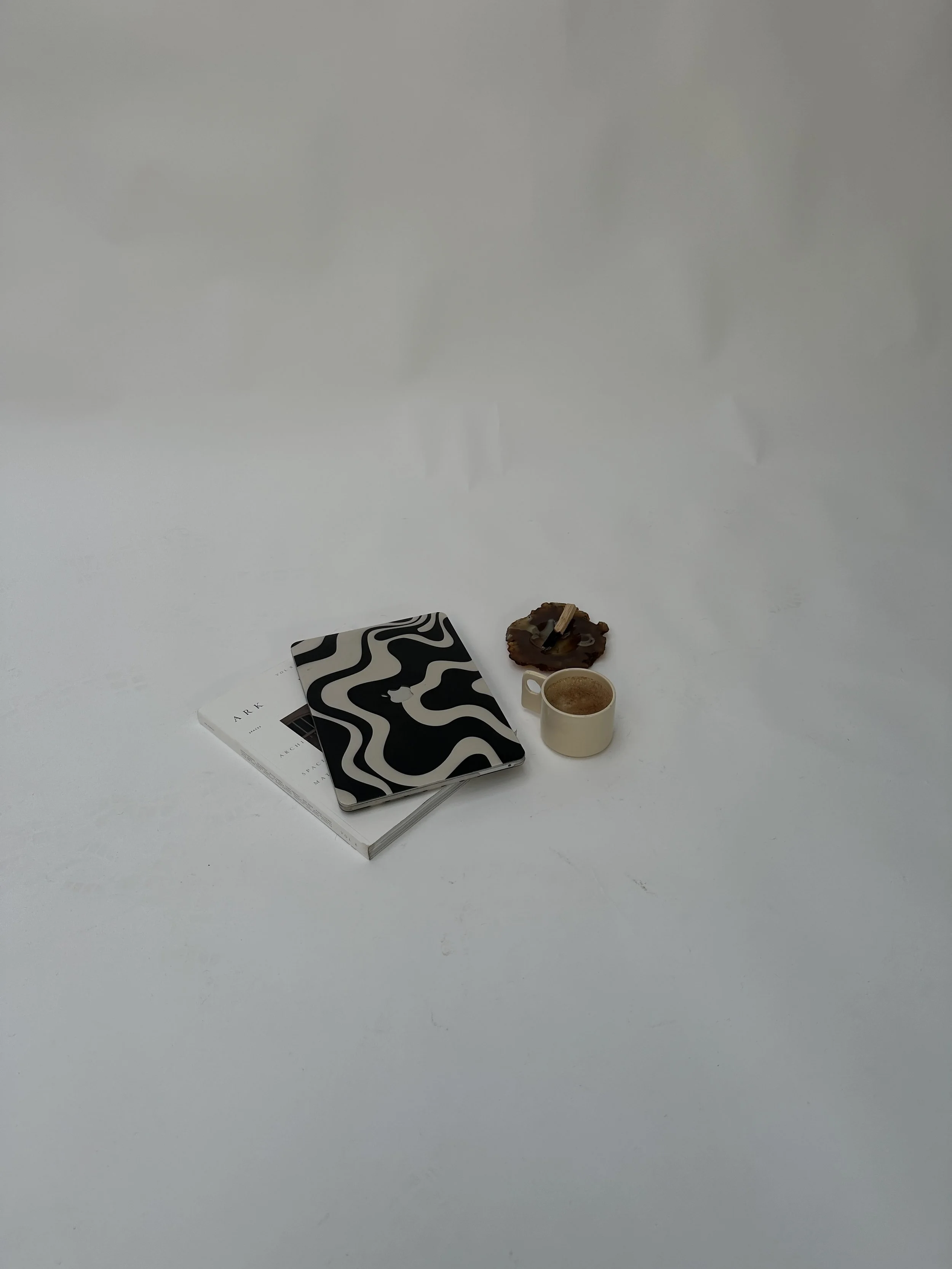 A white surface with a few books, a notebook, a cup of coffee, a piece of chocolate, and a small decorative object arranged in the lower center.