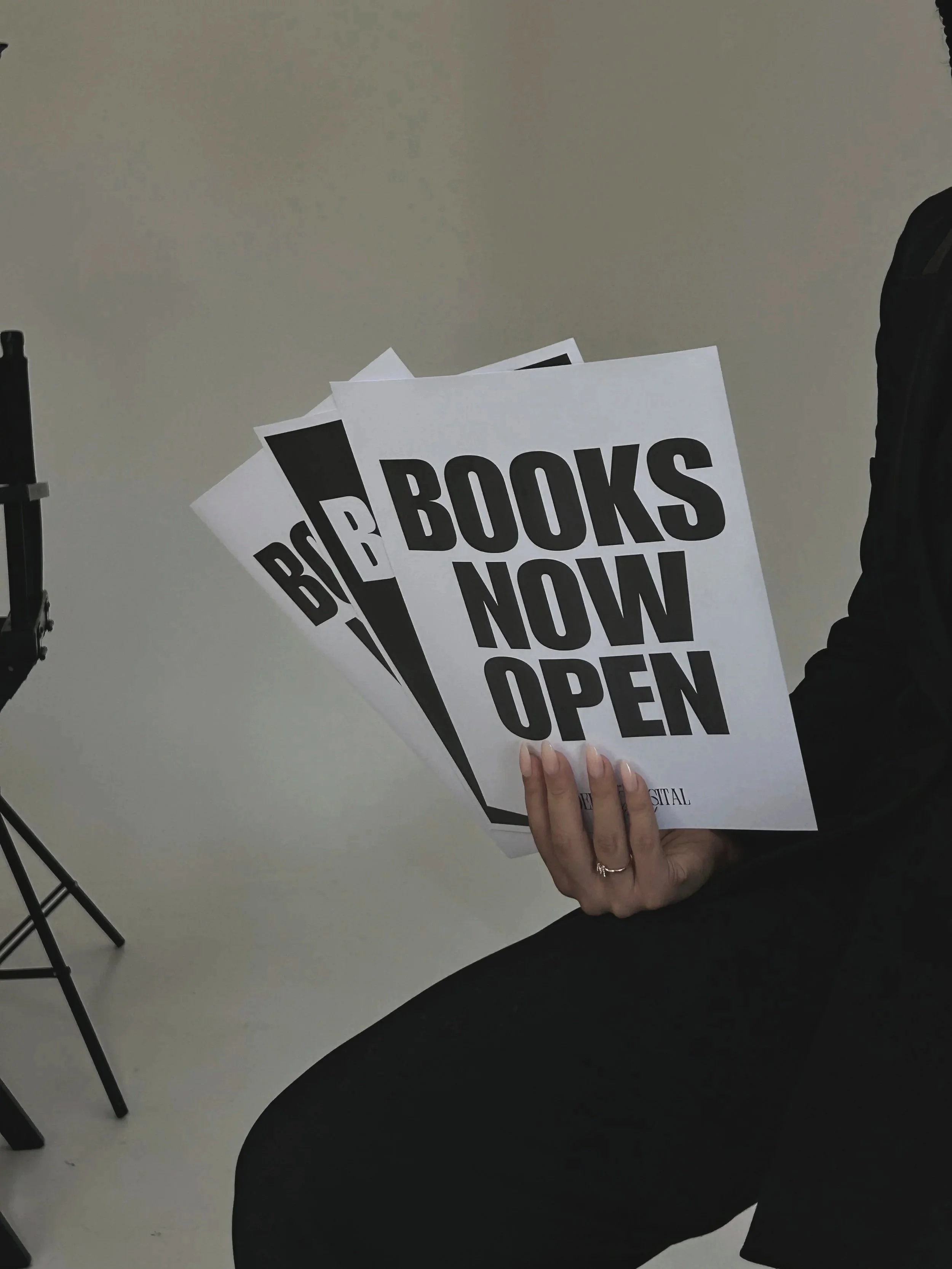 Person holding multiple signs that say 'BOOKS NOW OPEN' in black and white.