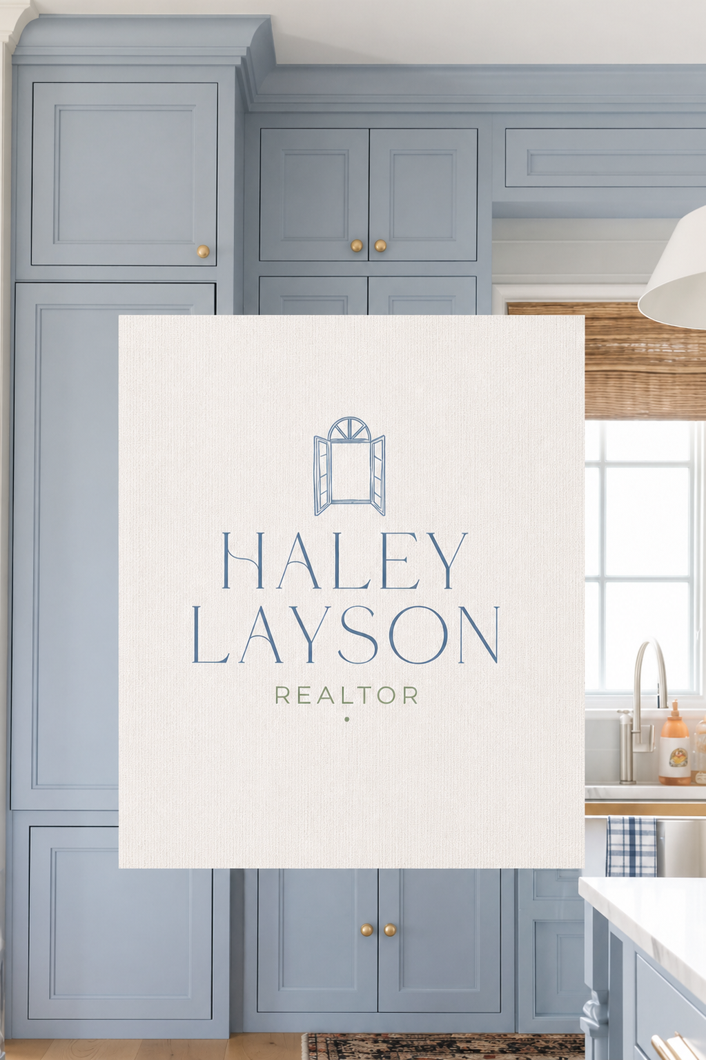 Sign for Haley Layson, Realtor, placed in a kitchen with blue cabinets and a window with a woven shade.