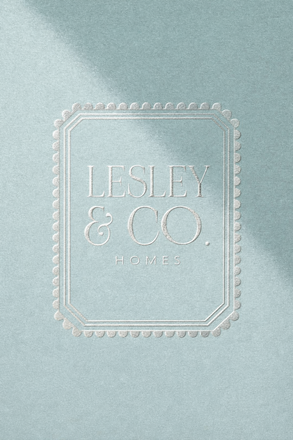 Light blue textured card with a decorative border featuring the text "Lesley & Co. Homes" embossed in white.