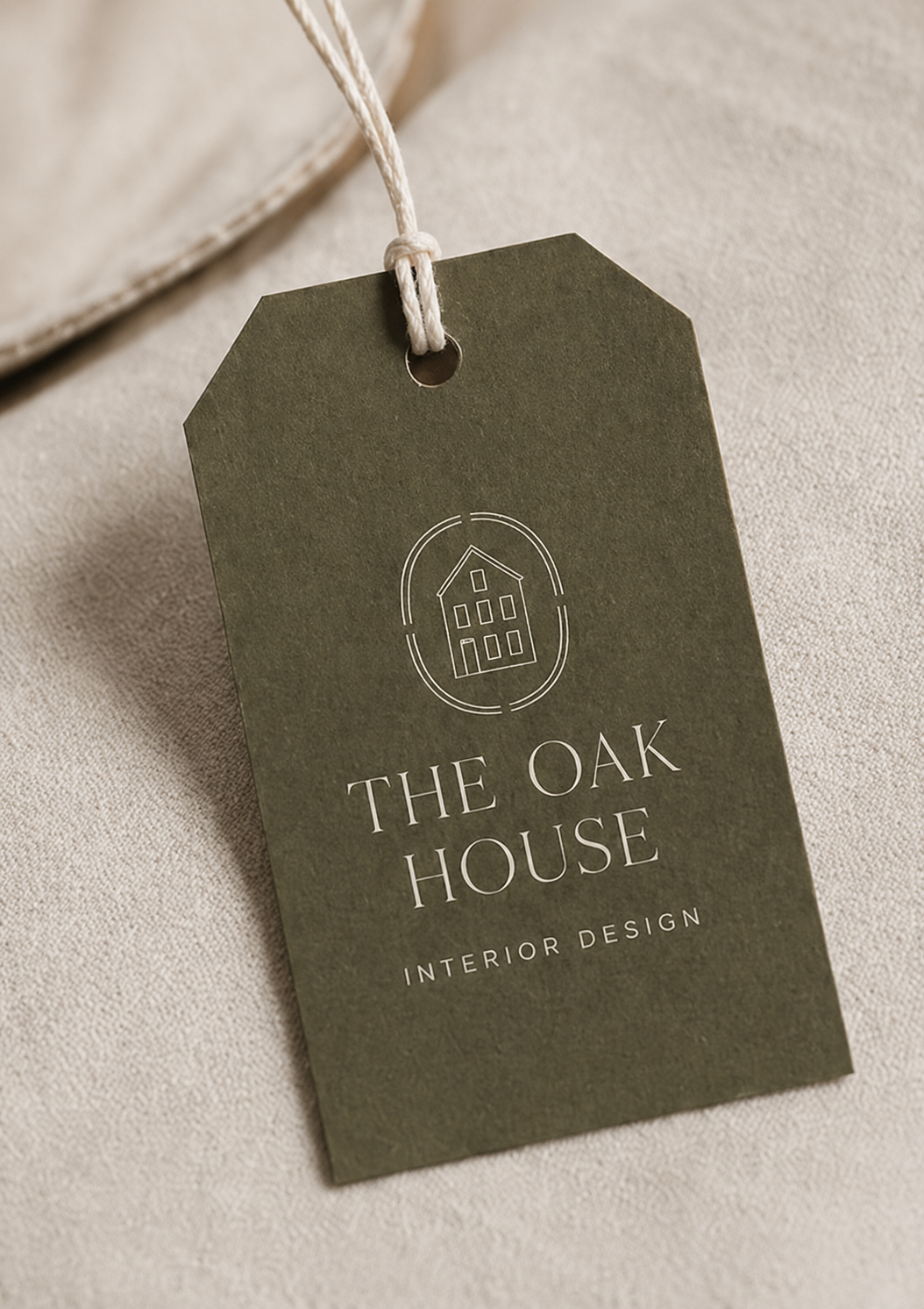A green tag with a simple line drawing of a house and the text "The Oak House" and "Interior Design" on a beige fabric surface.