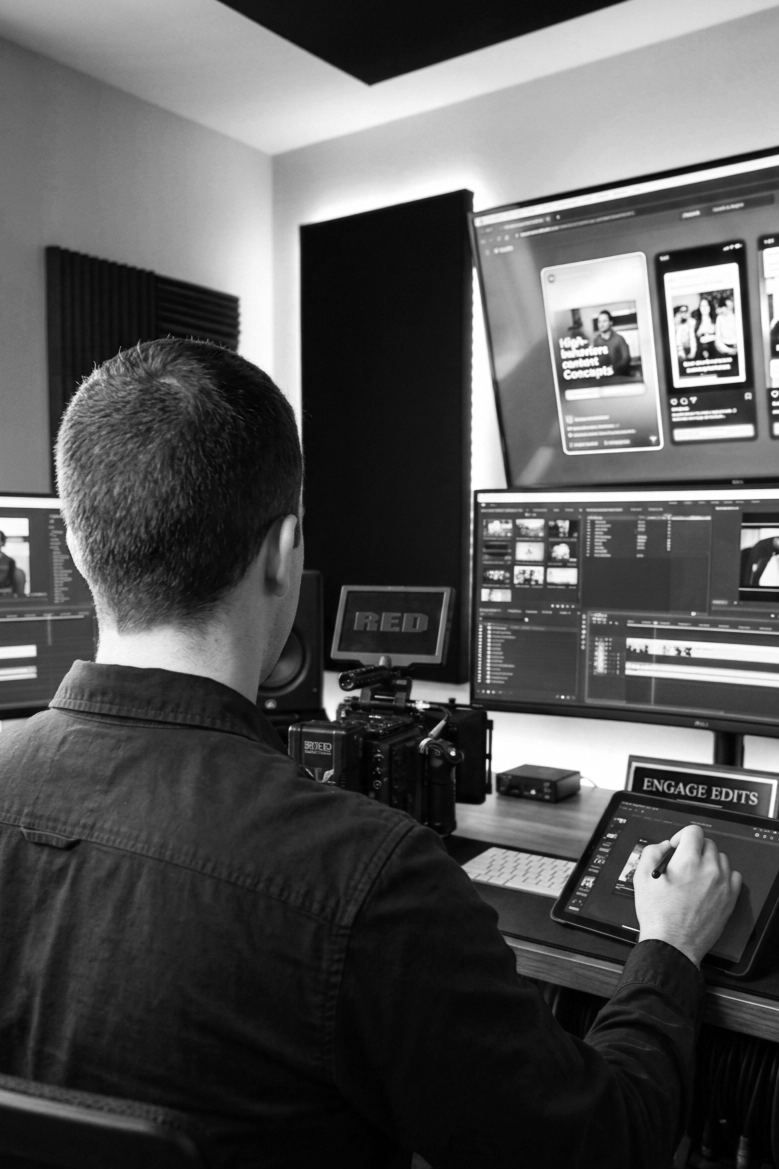 A person working in a video editing studio with multiple monitors displaying editing software, holding a pen and working on a touchscreen device.