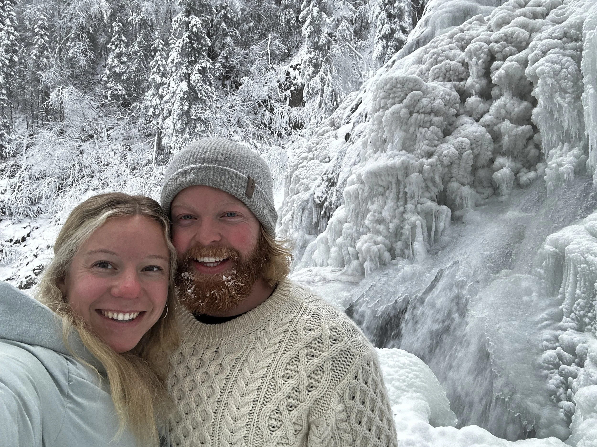 Family taking a selfie in front of a snowy, icy landscape with snow-covered trees and ice formations.