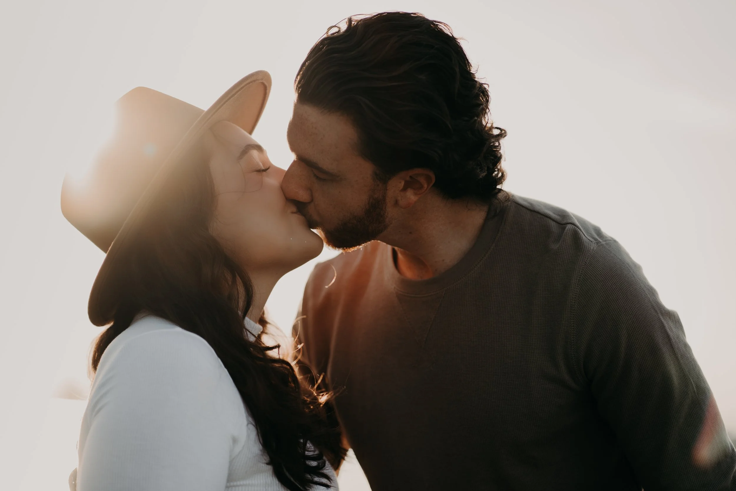 A couple sharing a kiss outdoors with the sun shining behind them.