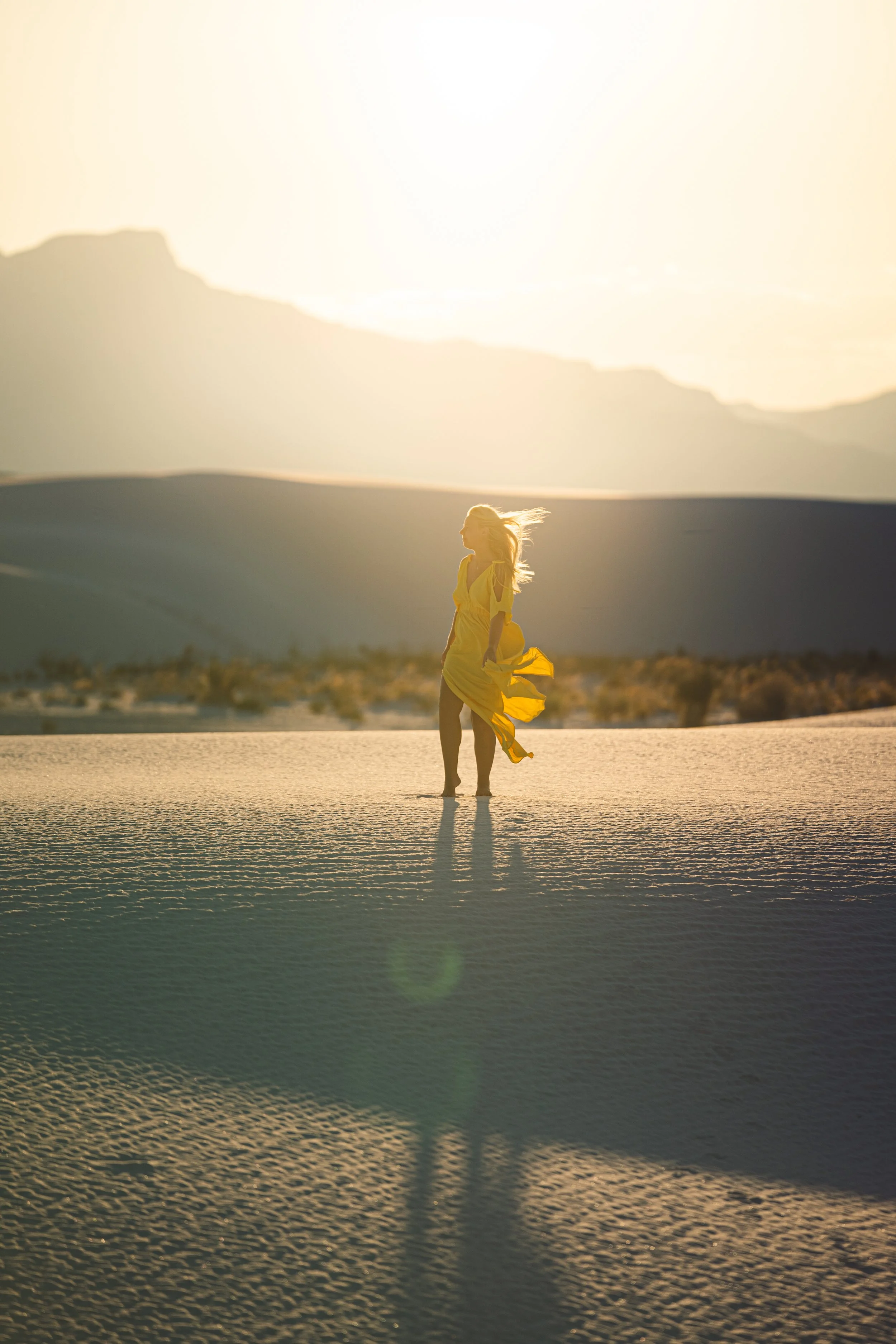 A woman in a yellow dress walking in a desert landscape at sunset.