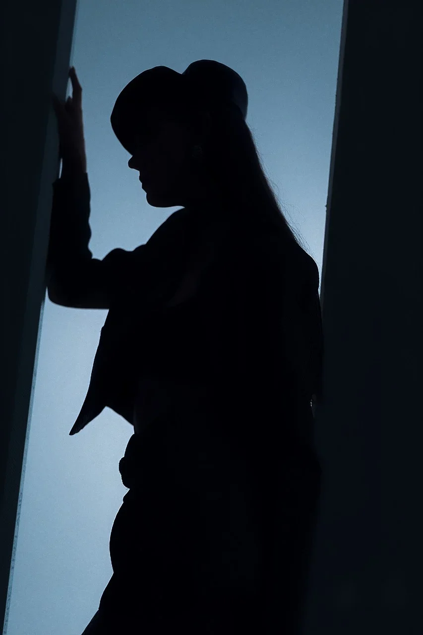 Silhouette of a woman wearing a hat, standing next to a door frame, with a blue-lit background.