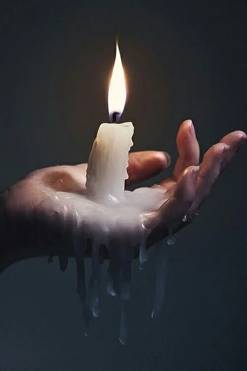 A hand holding a partially melted white candle with a burning flame, wax dripping down the hand.