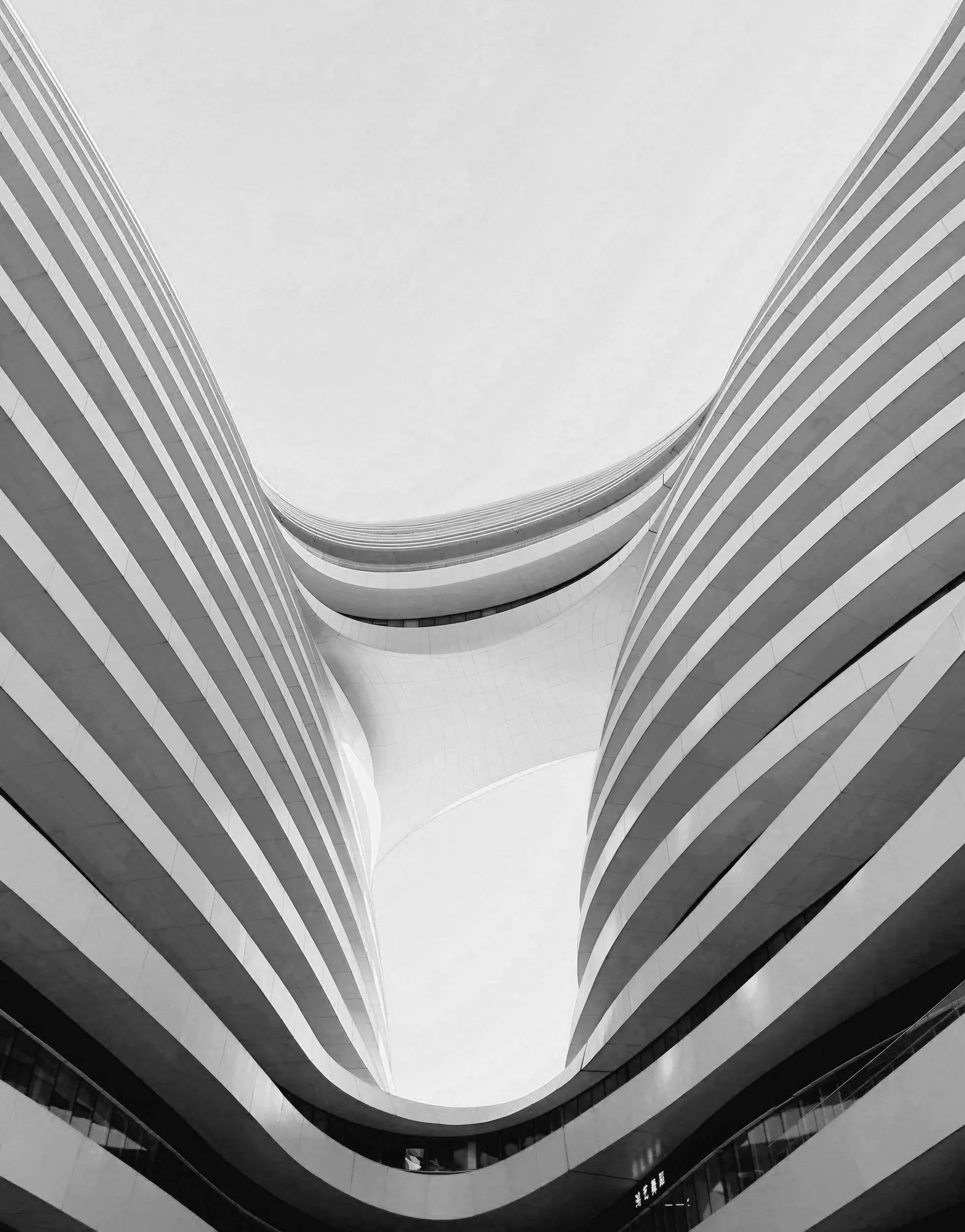 Looking up at the inside of a modern, multi-story building with curved, layered balconies that extend inward, creating a symmetrical, tunnel-like view.