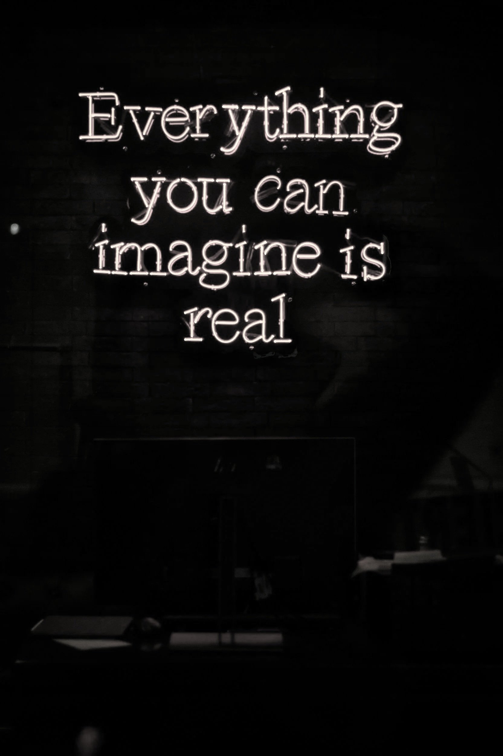Neon sign with the quote "Everything you can imagine is real" on a dark wall.