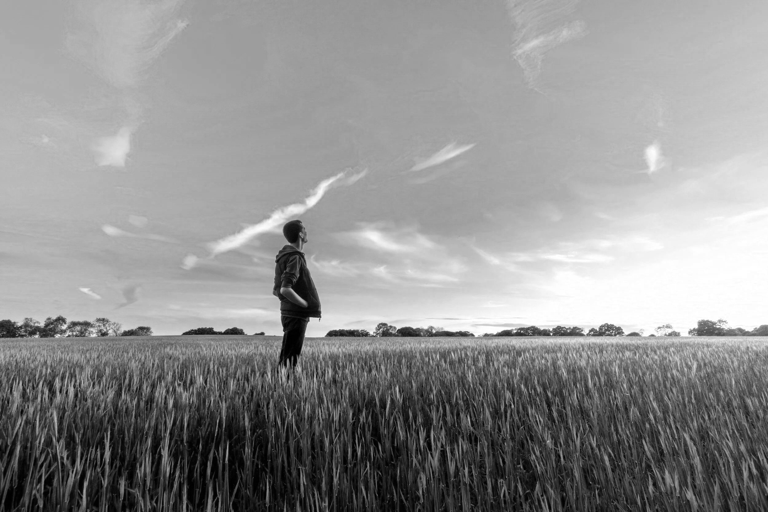A person standing in a field looking at the sky with clouds.