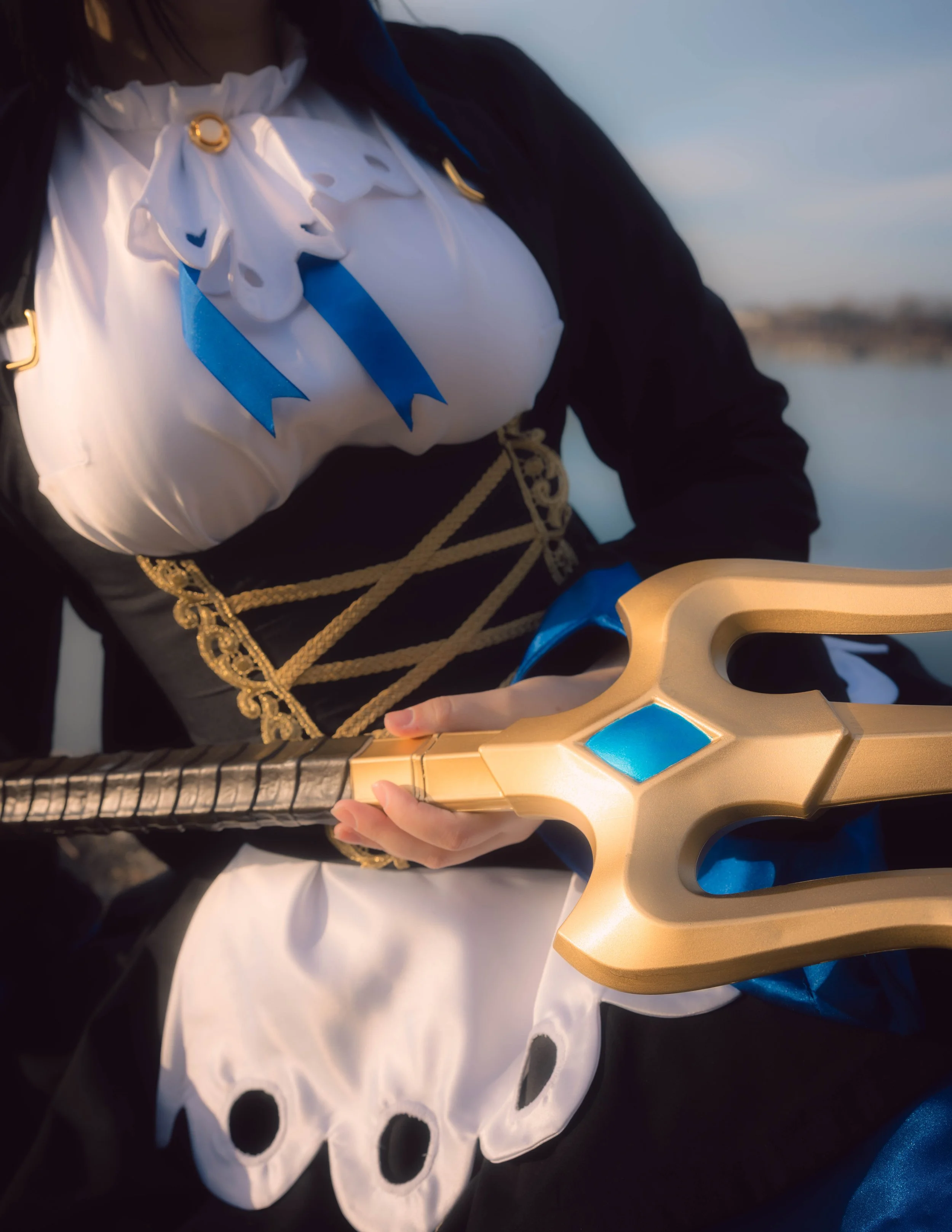 Close-up of a person dressed as a medieval knight, holding a sword with a gold and blue hilt, wearing a black and white costume with gold accents and a white ruffled collar.