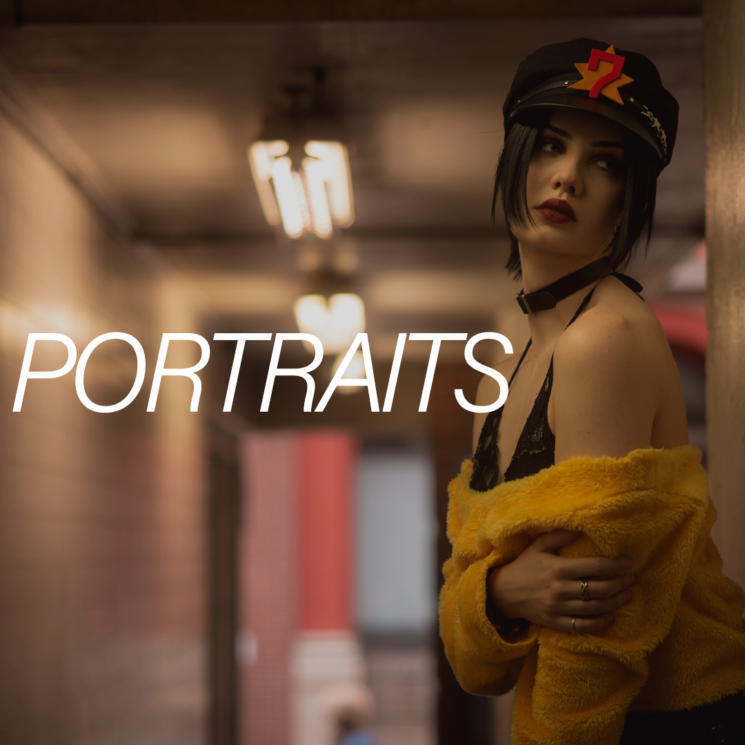 A young woman with dark hair wearing a black cap with a red and yellow number 7, a black choker, a yellow faux fur coat partially off her shoulders, and dark lipstick, standing in an indoor setting with blurred background lights and brick walls.