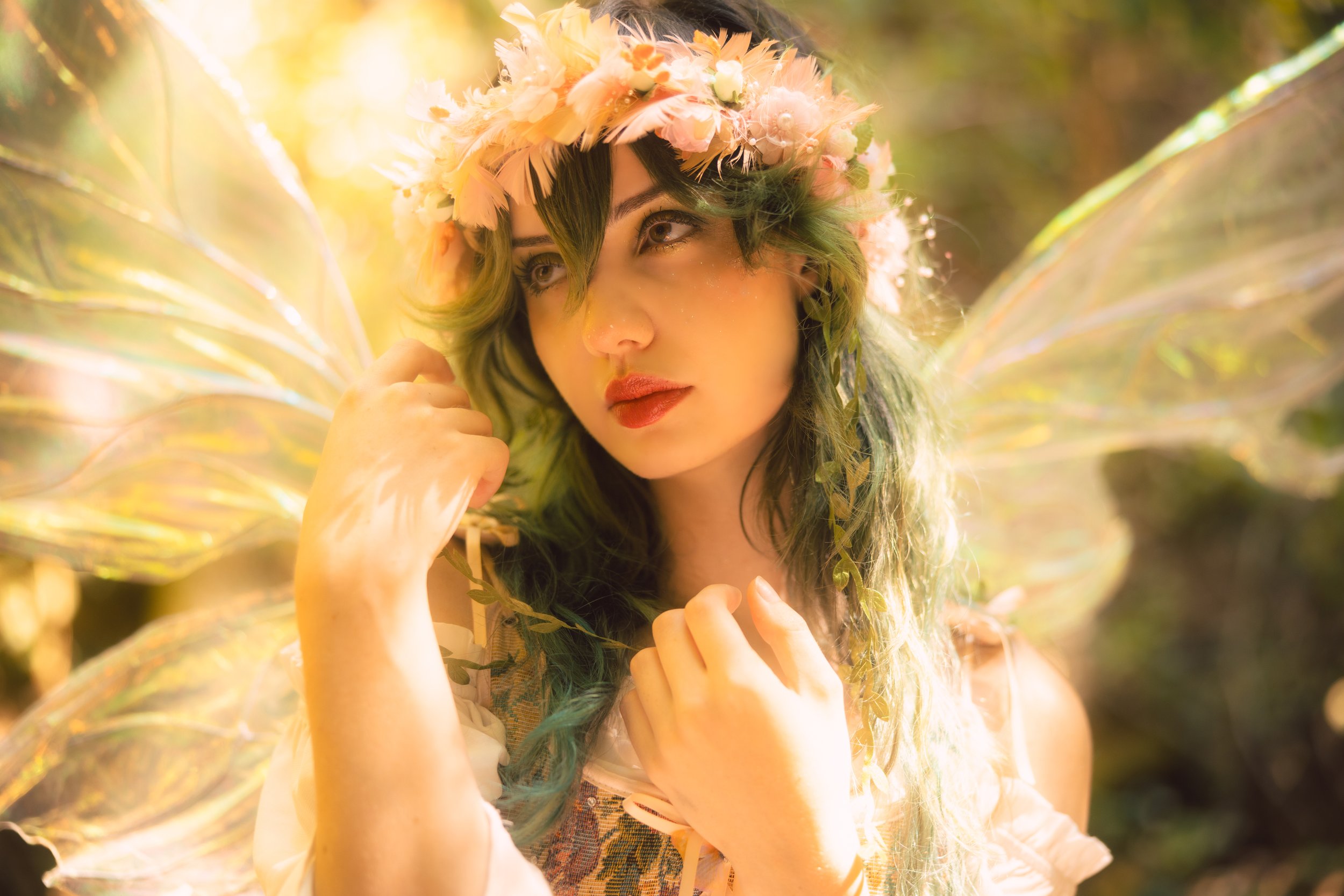 A woman wearing a flower crown with pink and peach flowers, surrounded by sunlight and green leaves, with iridescent wings behind her.