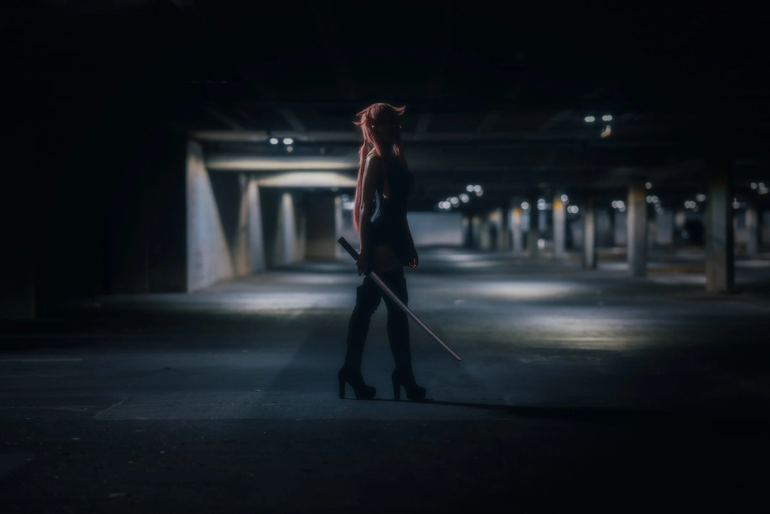 A woman with long pink hair and high-heeled boots walking with a sword in an empty, dark parking garage.