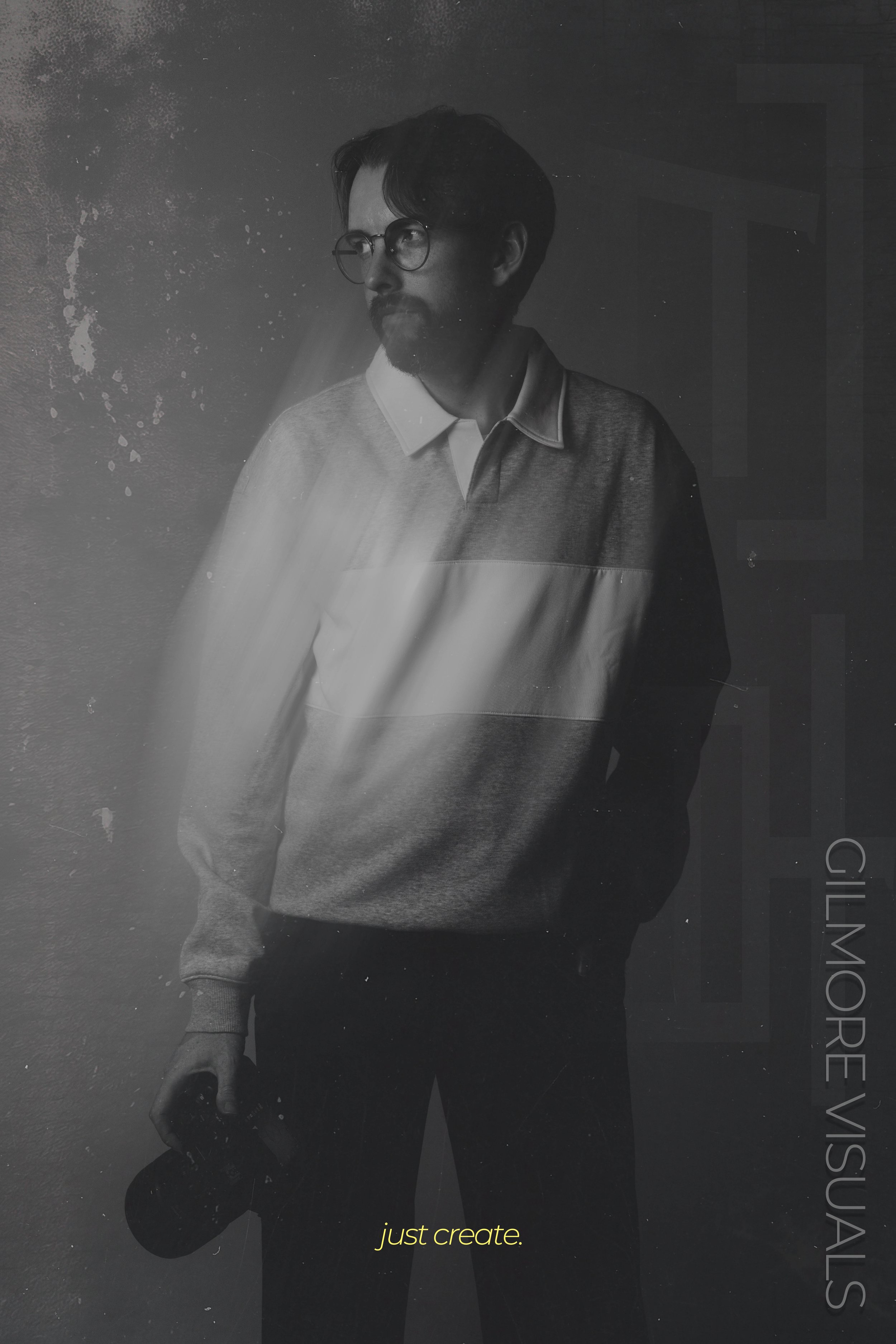 A black and white photo of a man with glasses and facial hair wearing a collared shirt under a sweater, looking to the side. Text at the bottom reads 'just create.'