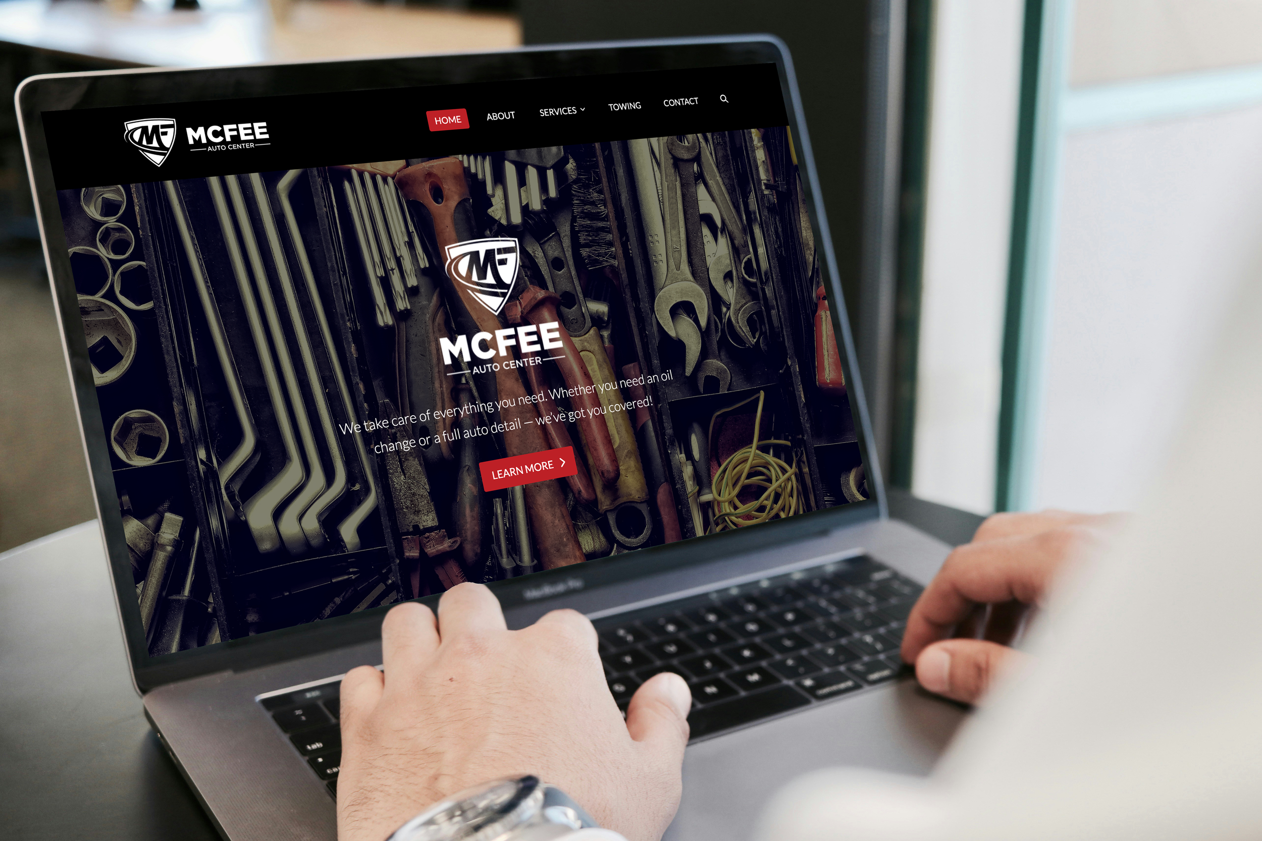 Person using a laptop to view the homepage of MCREE Auto Center website, which features a background image of various tools.