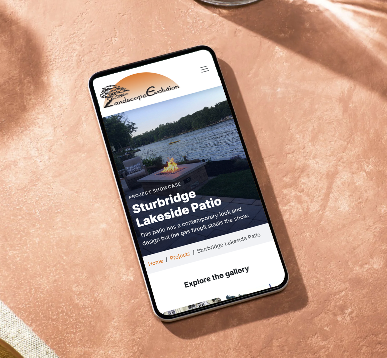 A smartphone displaying a webpage for Landscape Evolution, featuring a project called Sturbridge Lakeside Patio with an image of an outdoor patio and lake in the background.