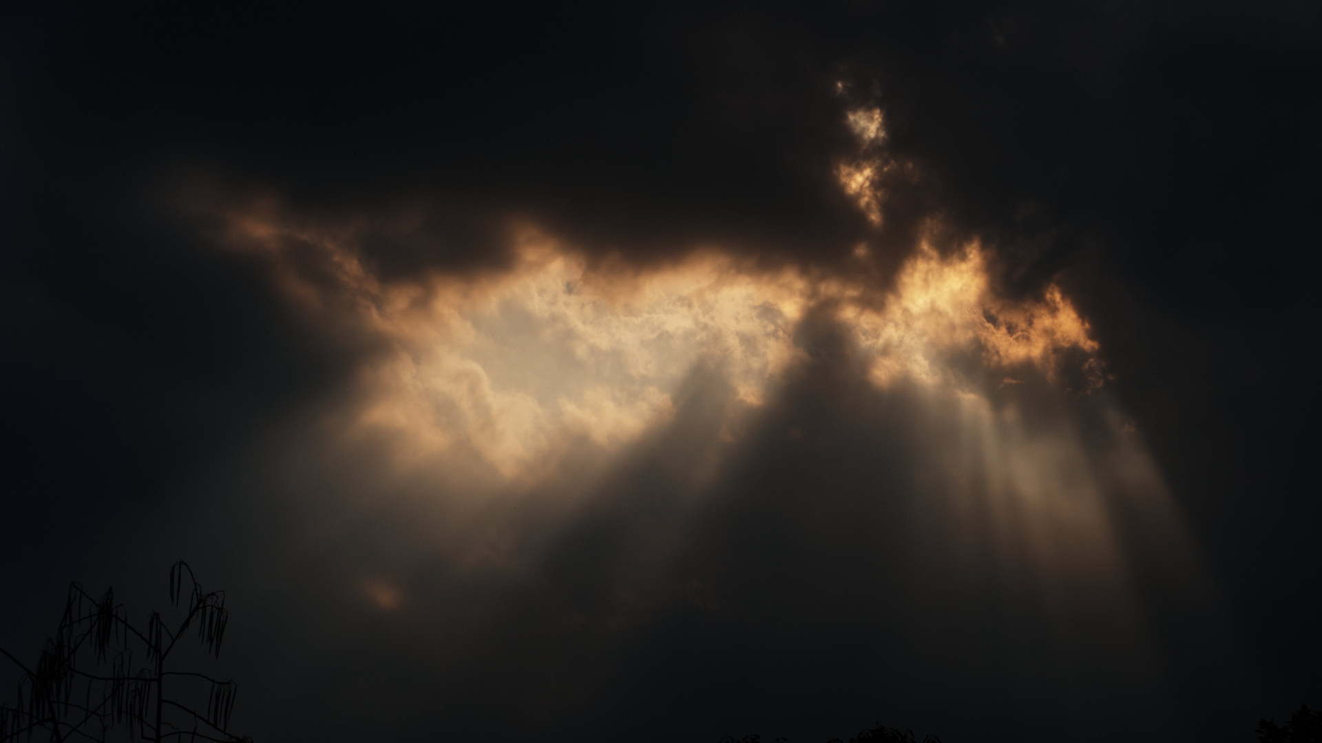 Dark clouds in the sky with rays of sunlight breaking through.