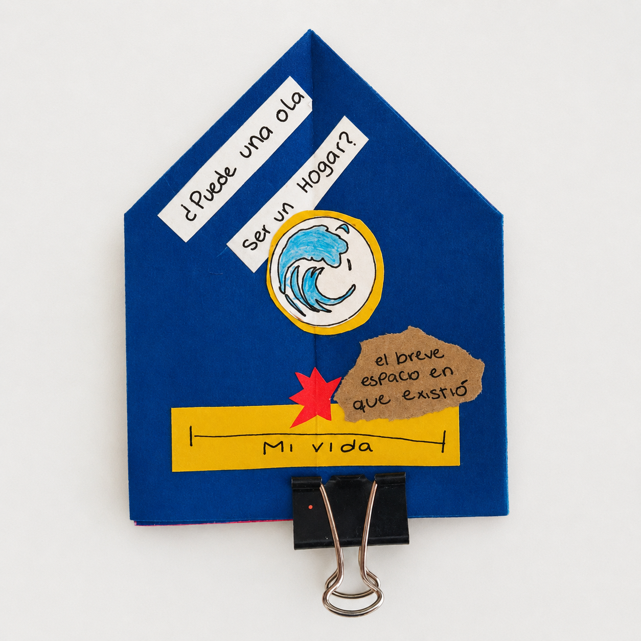 Blue paper house-shaped craft with Spanish text, a drawing of a wave, a yellow bar labeled 'Mi vida,' and a red star, held by a black clip.