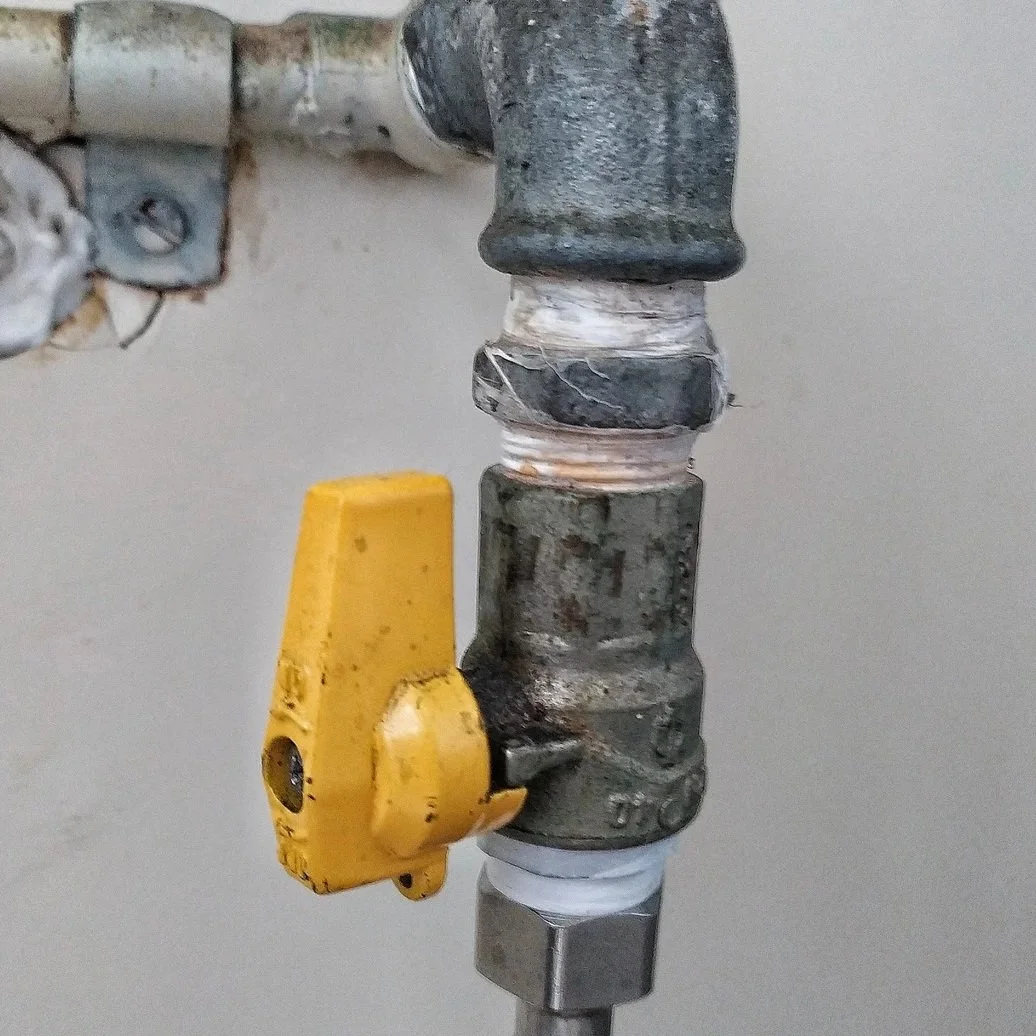 Corroded under-sink shutoff valve with yellow handle and braided supply line showing aging plumbing connection requiring replacement service.