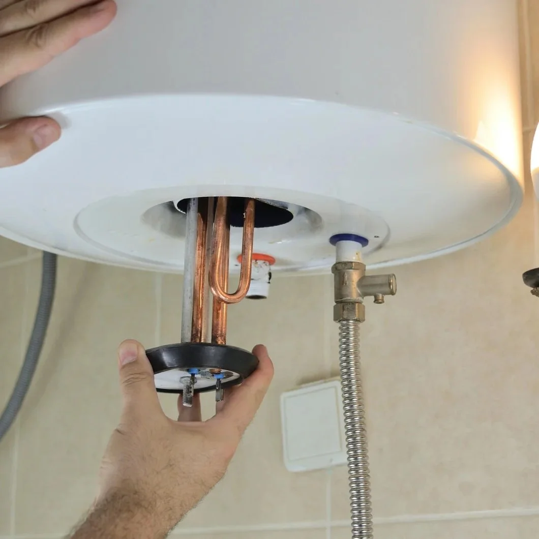 Technician installing residential tank water heater with exposed heating components and plumbing connections during professional hot water system setup.