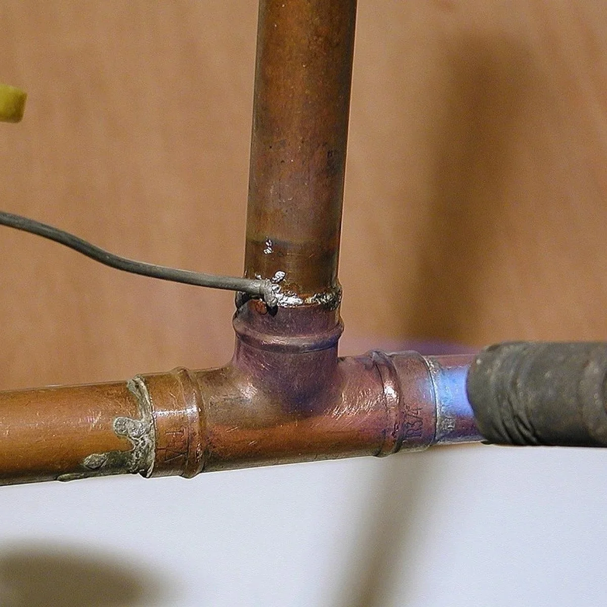 Plumber soldering burst copper pipe repair during emergency water leak service to prevent structural water damage inside home.