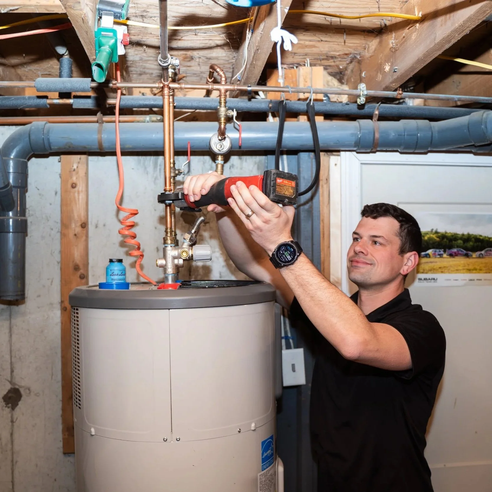 Plumber servicing residential water heater and plumbing connections during replacement installation in Maine basement utility area.