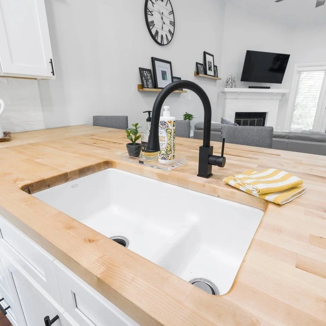 White farmhouse kitchen sink with black faucet and butcher block countertop during plumbing finish installation preventing future drain leaks issues.
