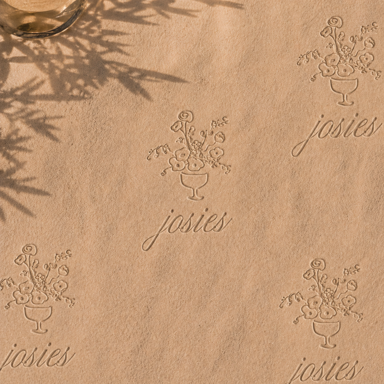 Embossed pattern on tan paper featuring a floral design in a goblet and the word 'josies' repeated multiple times.