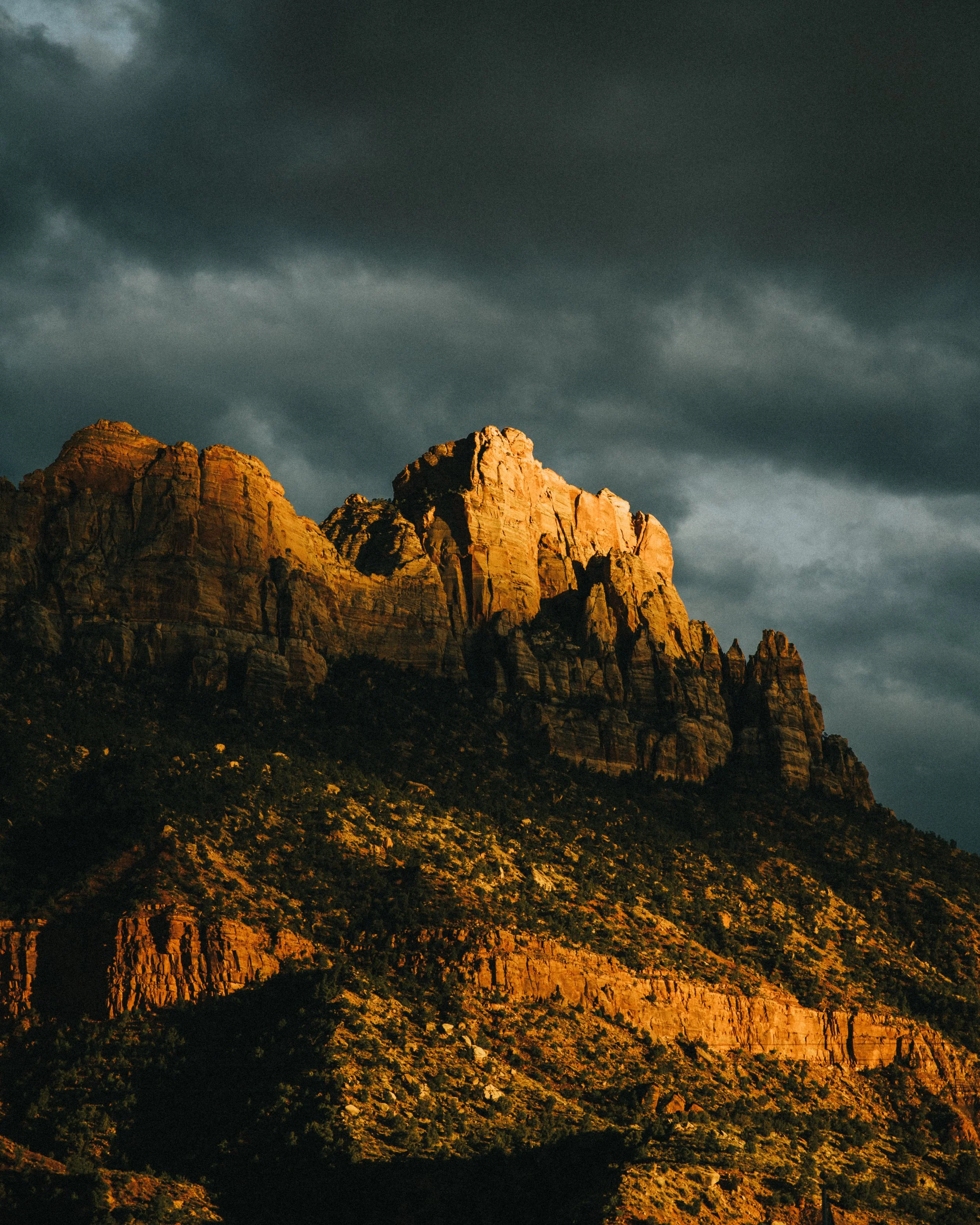 Sunlit mountain cliffs against a dark, ominous cloudy sky.
