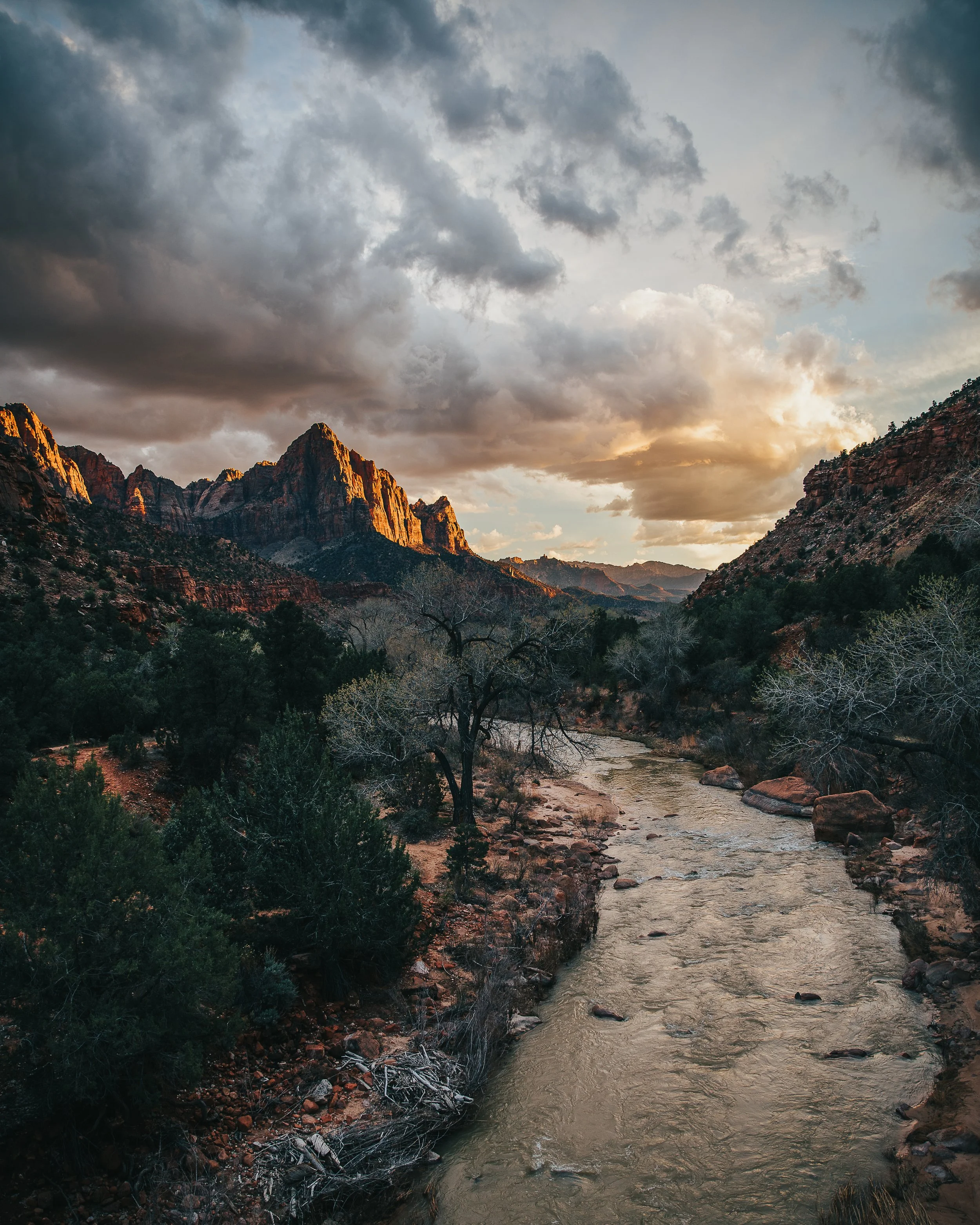 Sunset over rugged mountains with a river flowing through a forested valley.