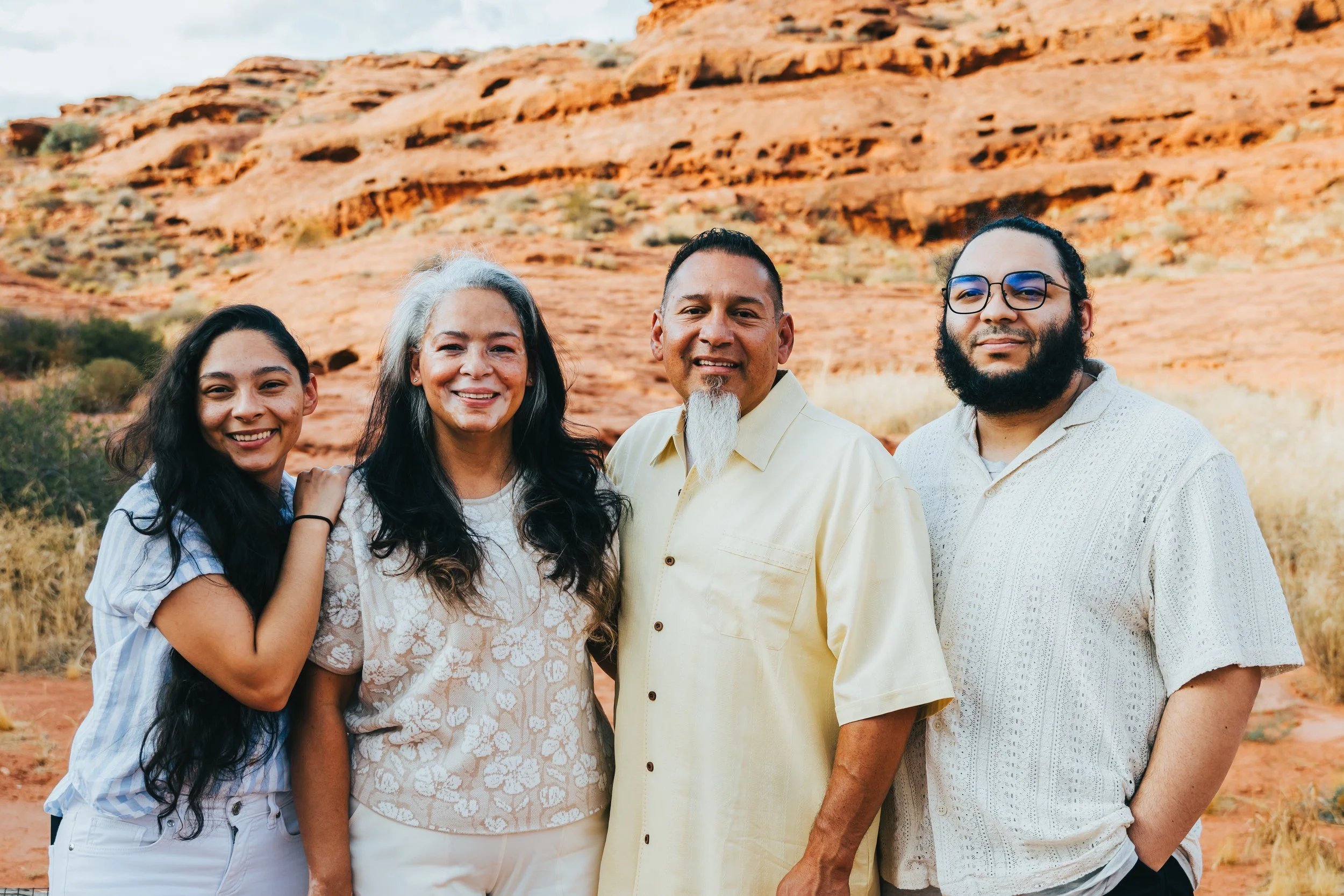 Group of five diverse people standing together outdoors with a red rocky desert landscape in the background.