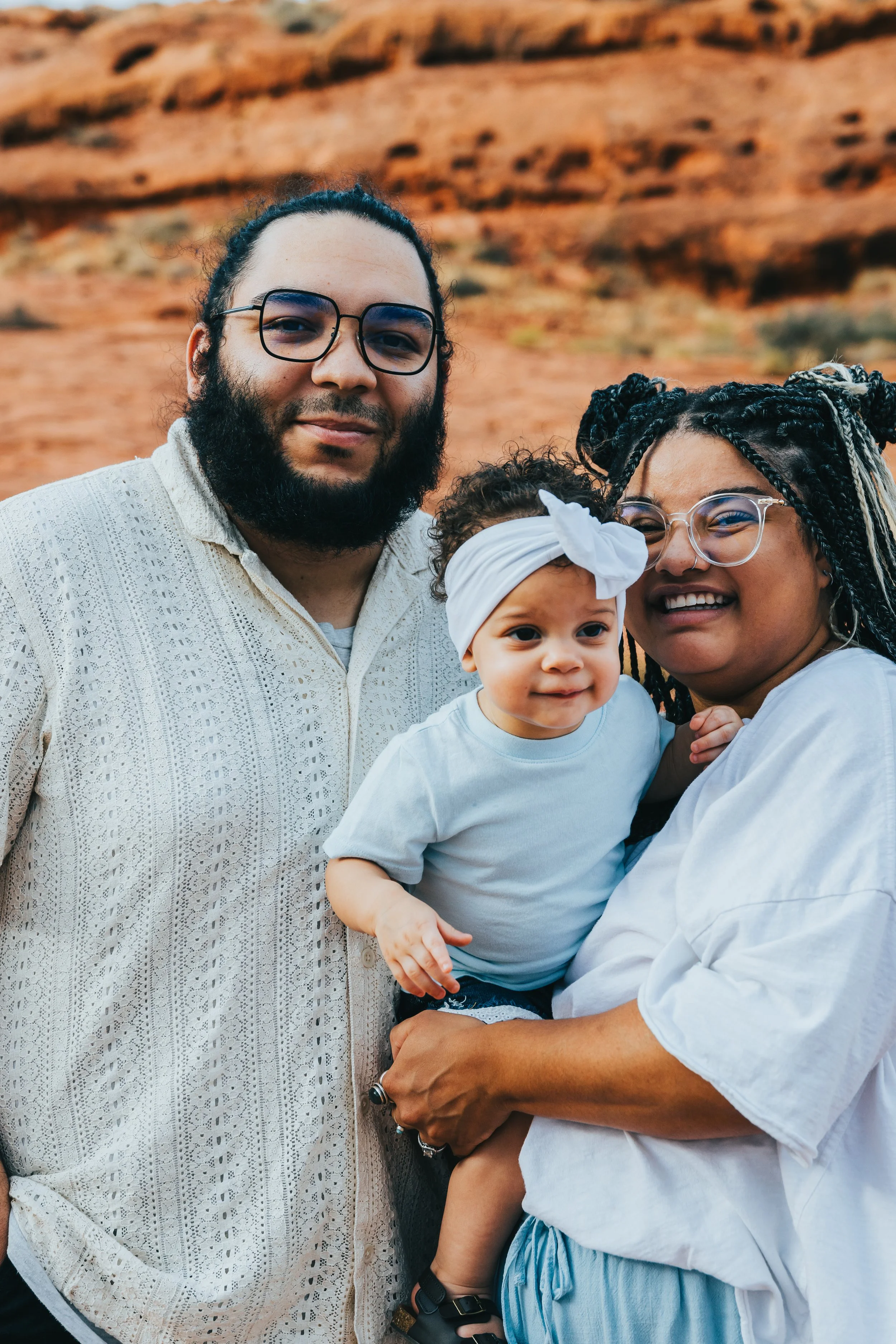 A group of three diverse people smiling outdoors with a rocky, desert-like background.