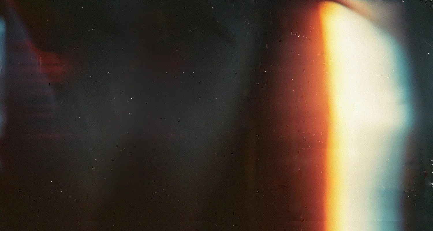 An abstract image with dark and light areas, featuring a gradient of warm colors like orange, red, and yellow on the right side and darker tones with specks of light on the left side.