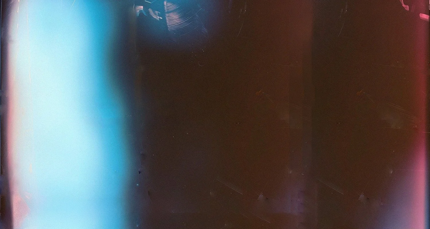 The image is mostly dark and features a mix of colors including pink, blue, and purple. There appears to be some reflections or light streaks, giving an abstract and slightly blurry appearance.